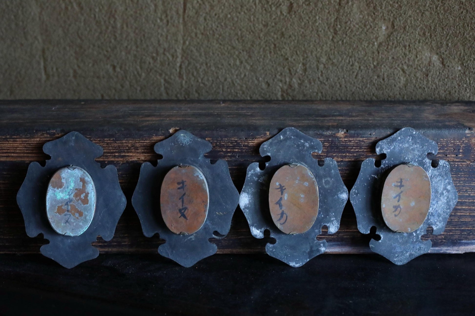 a collection of four oval-shaped metal objects with Japanese characters on them, arranged in a row on a wooden surface.