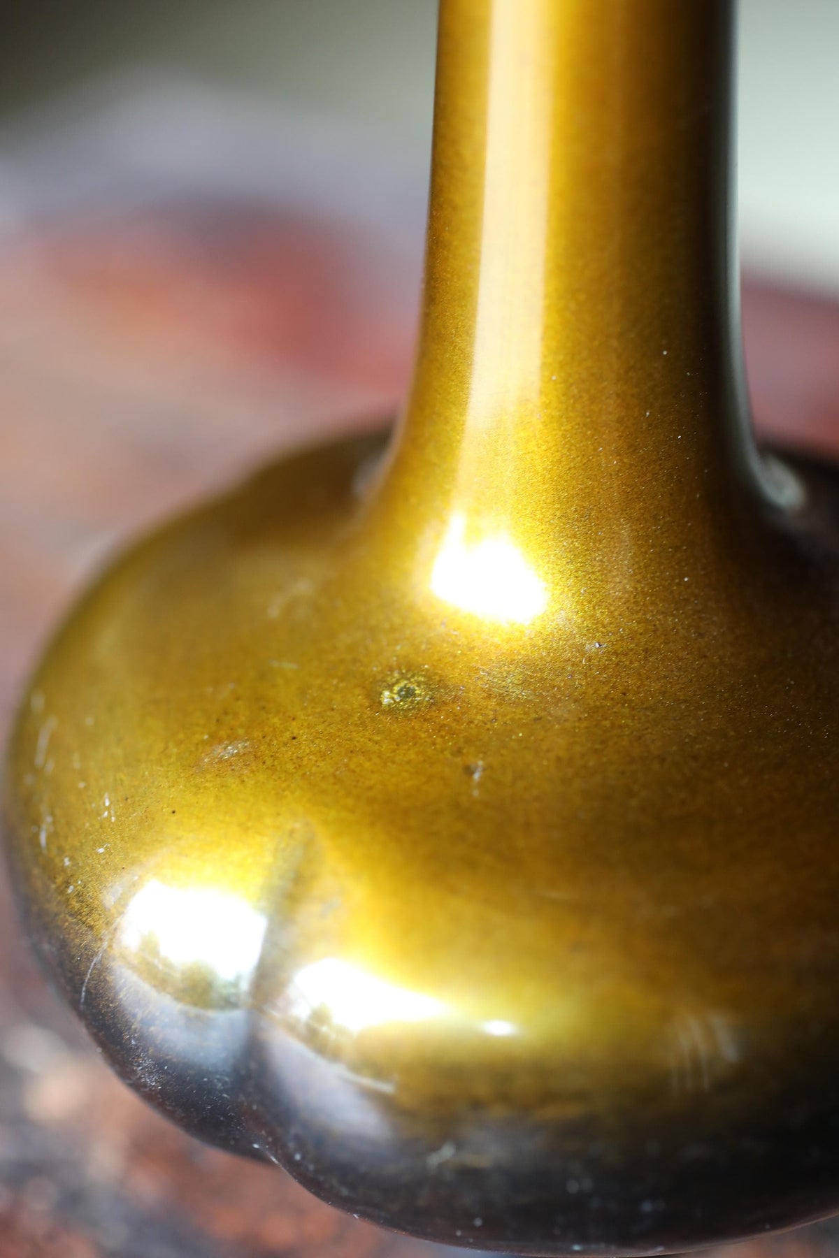 A close-up view of a shiny, golden-colored vase or container with a small hole or opening in the center.
