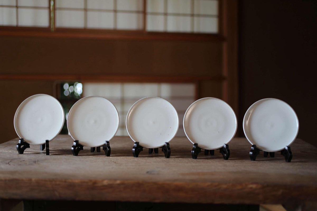 A row of five white plates stands on a wooden table, each plate standing on a black stand.