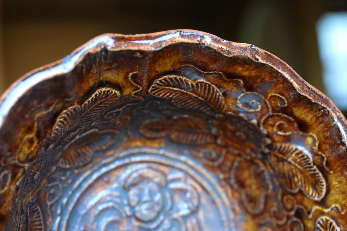 A close-up view of a decorative ceramic bowl with intricate patterns and designs, including leaves and floral motifs.