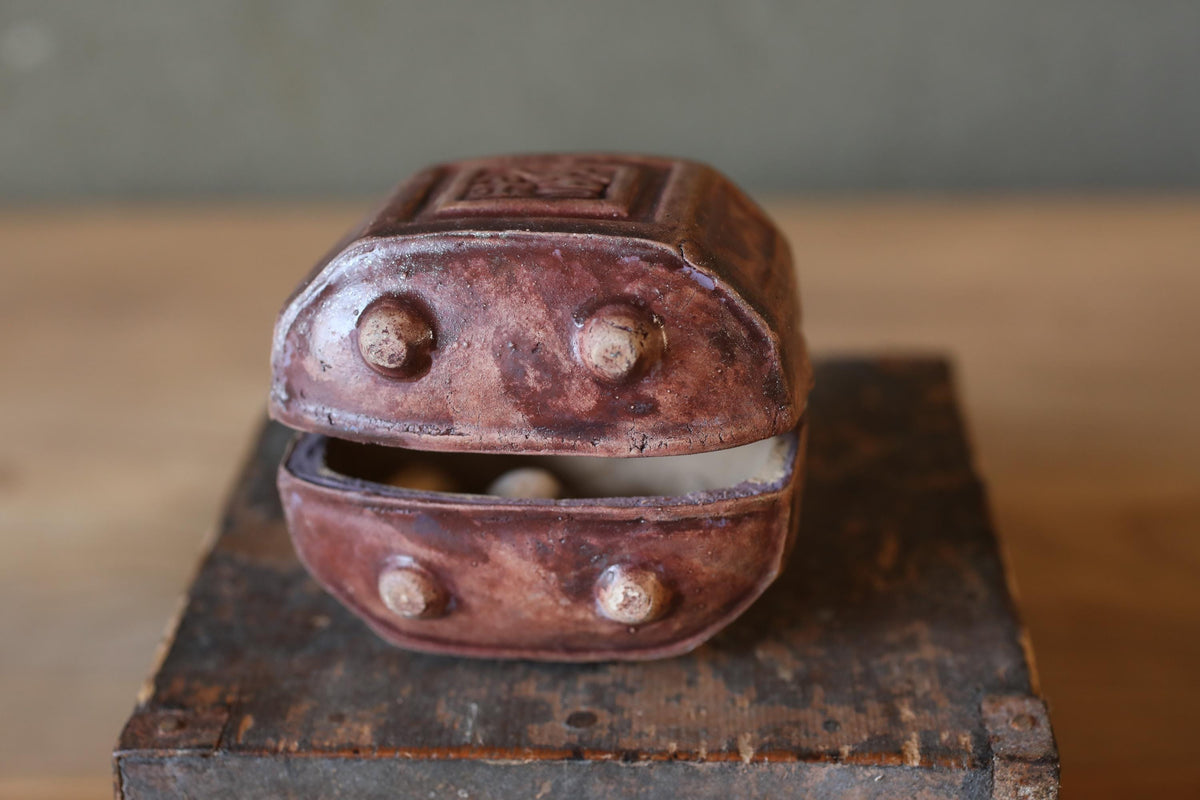 An old, rusted metal box with a carved design on the top sits on a wooden surface.