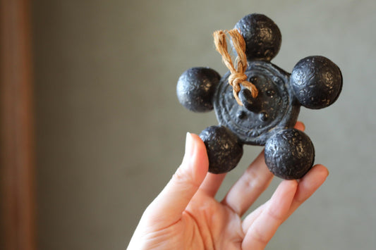 A hand holding a small, black metal object with six round balls attached to it.