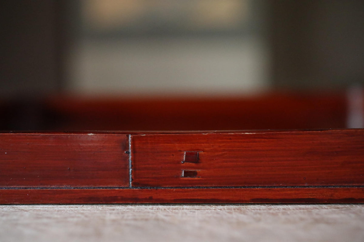 A close-up view of a wooden surface with a dark red or brown color, featuring a small, dark-colored detail or mark on the surface.