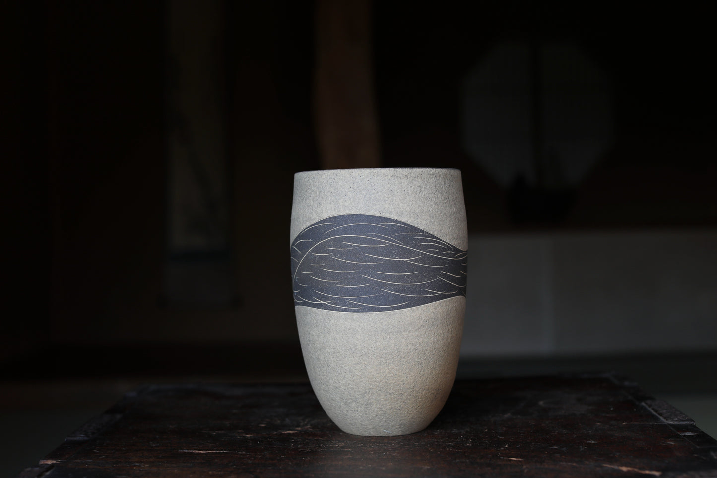 A white ceramic vase with a blue leaf design on it, placed on a dark wooden surface.
