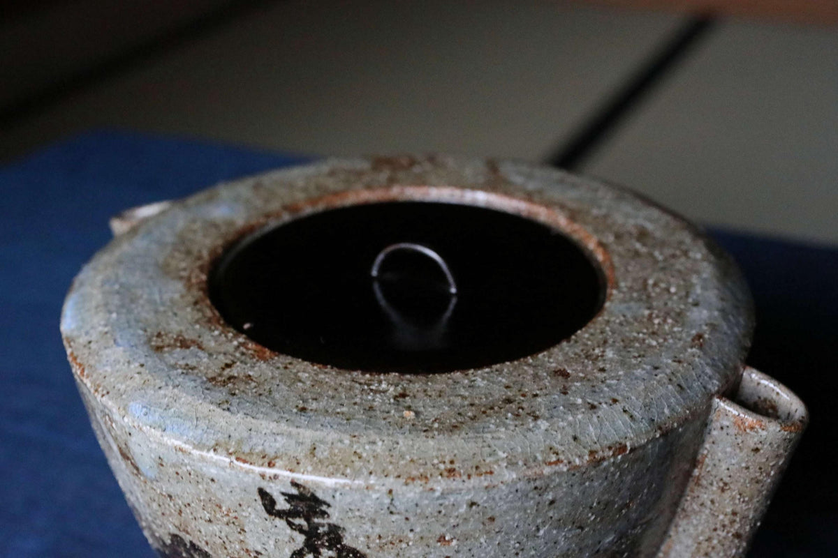 A close-up view of a ceramic teapot with a dark liquid inside, placed on a blue surface.