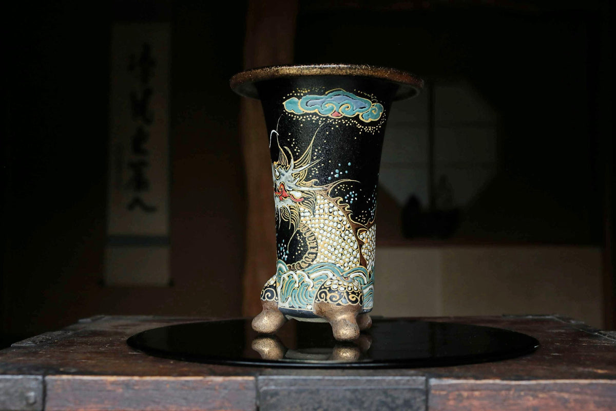 A decorative black vase with a dragon design on it, placed on a wooden surface.