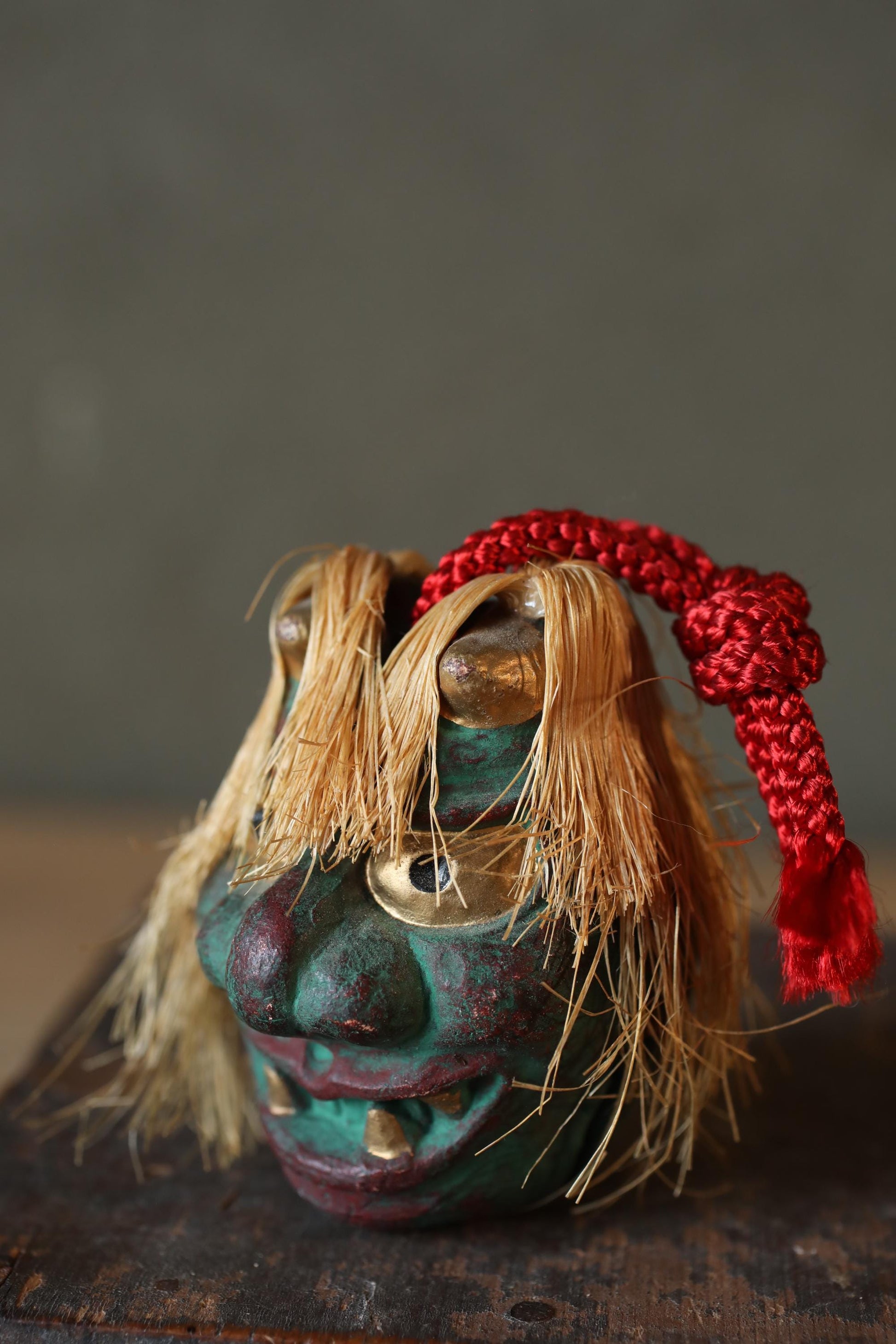 A colorful, intricately designed mask with a red string around its neck, sitting on a wooden surface.
