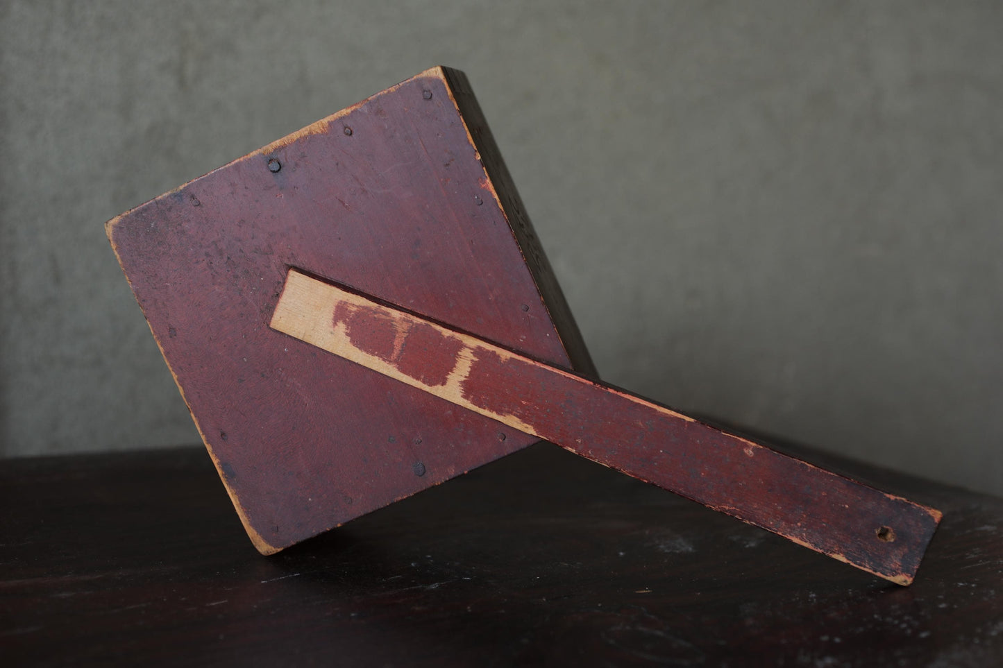 a wooden object with a reddish-brown finish, resting on a dark surface.