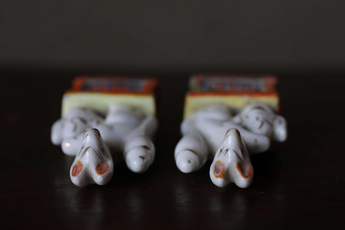 Two ceramic figurines with orange and white accents are arranged on a dark surface.