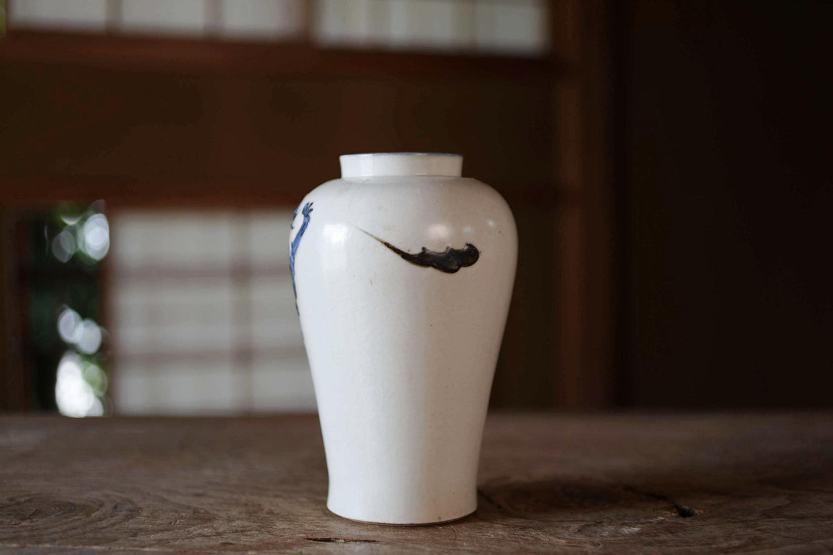 A white ceramic vase with a black design on it, placed on a wooden surface.