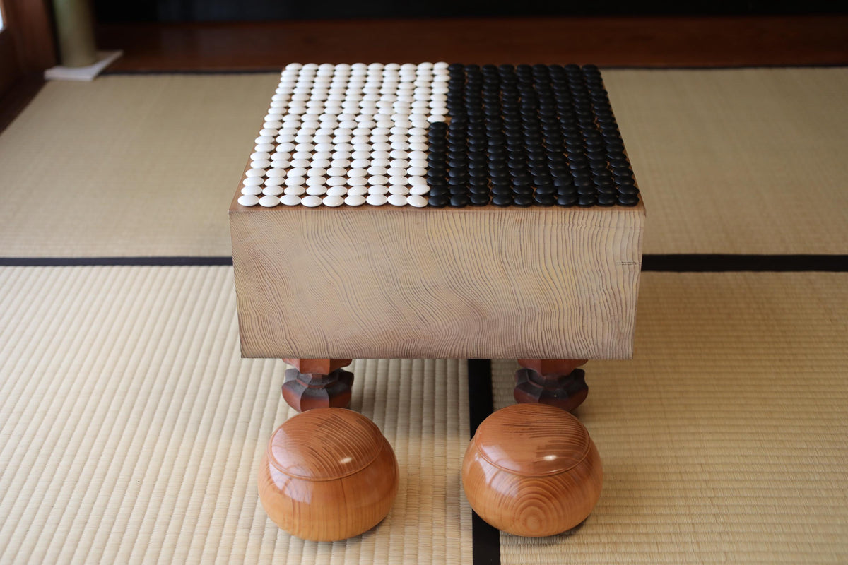 a wooden table with a unique design, consisting of a square top and bottom, and two wooden legs. The table is placed on a tatami mat, which is a traditional Japanese floor covering.
