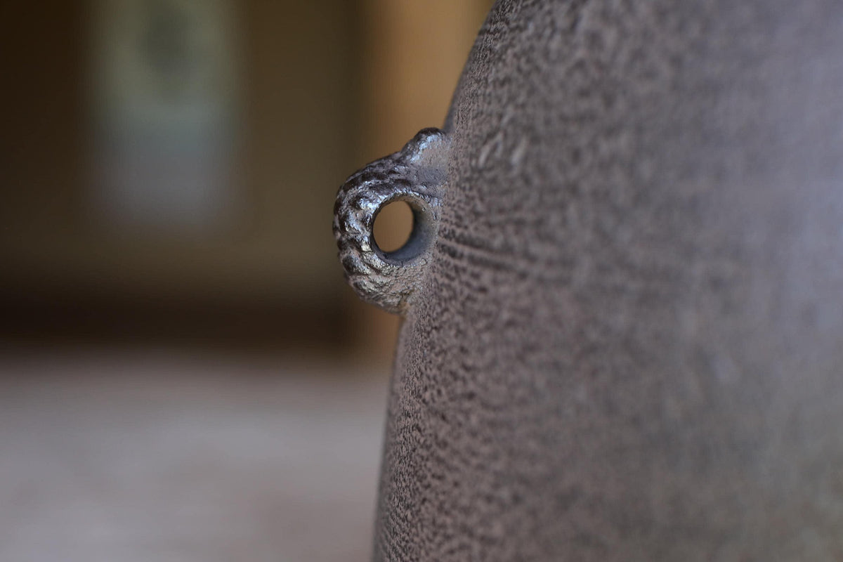 A close-up view of a textured surface, possibly a piece of pottery or a wall, with a small hole or opening in the center.
