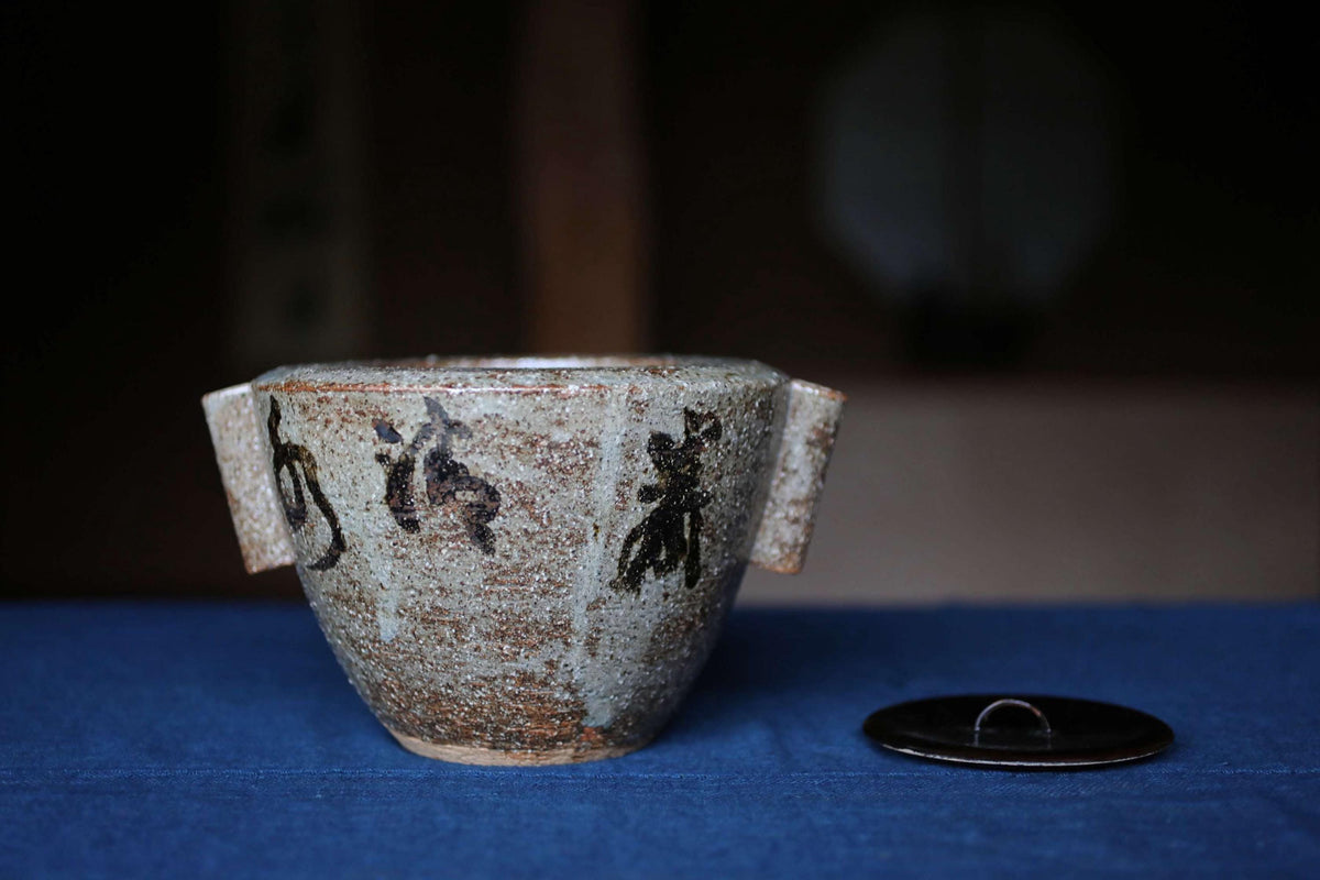 A ceramic bowl with a lid, placed on a blue surface, with a blurred background.
