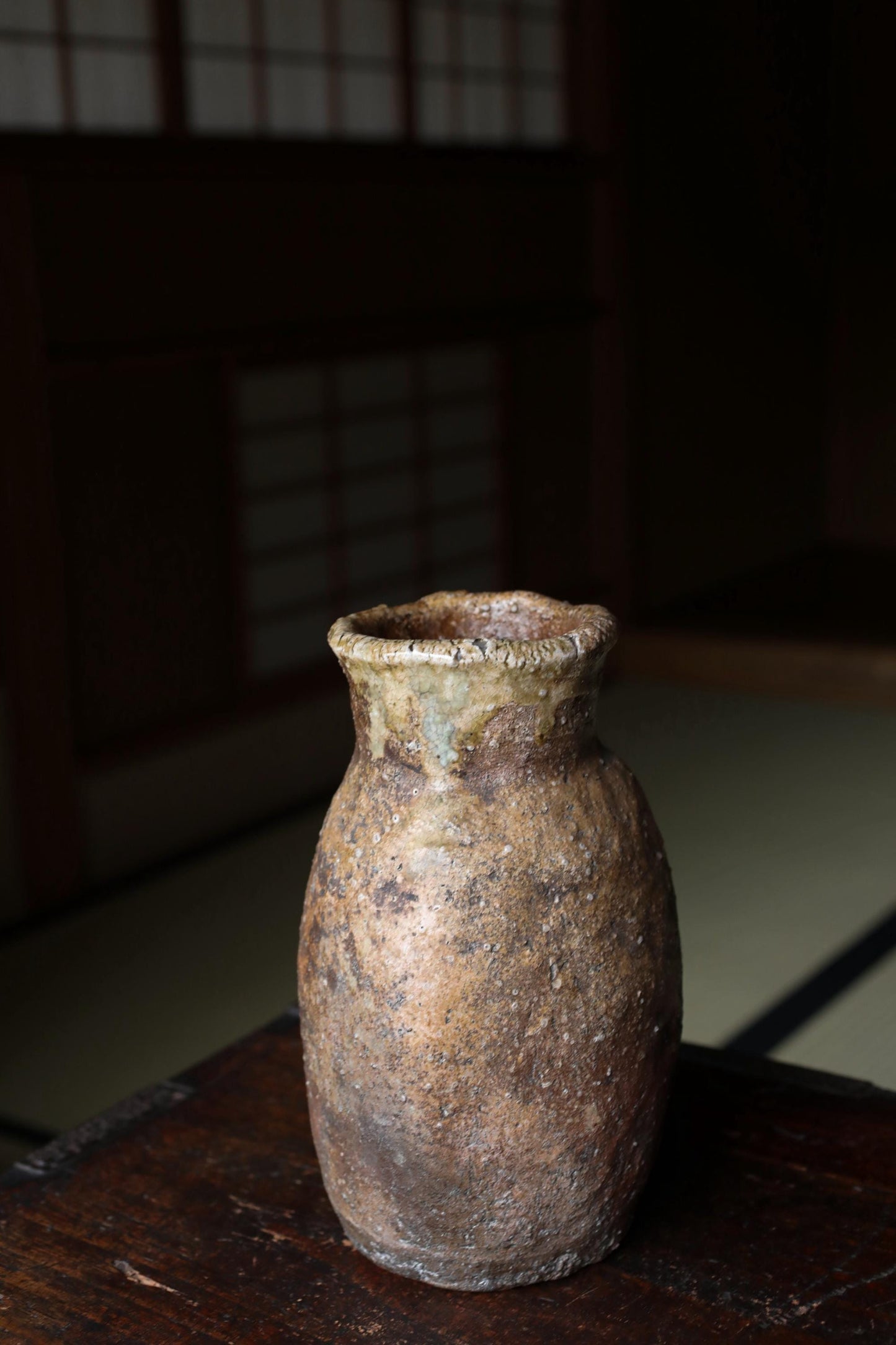 An old, weathered ceramic vase sits on a wooden surface, its surface showing signs of age and use.