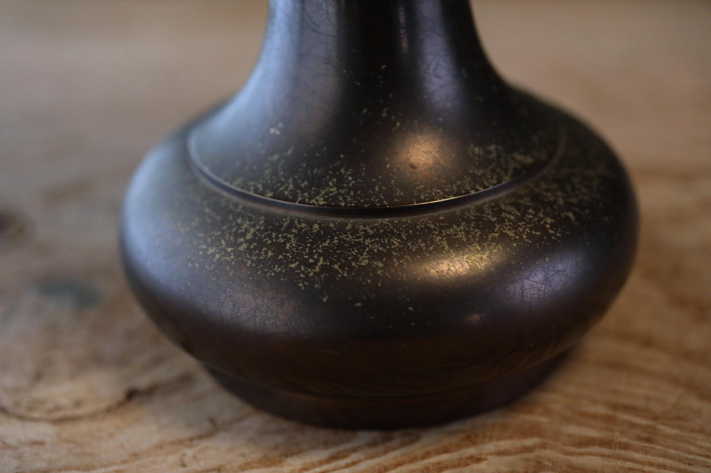 A close-up view of a dark, textured vase or container with a shiny, reflective surface.