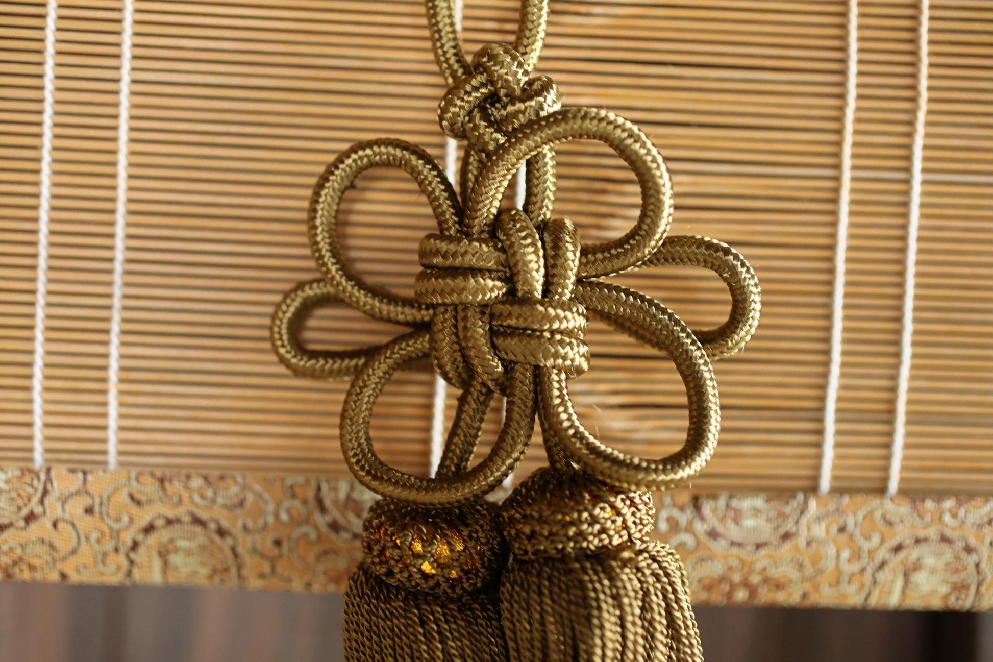 A decorative gold-colored tassel or fringe hanging from a bamboo or wooden blind, creating an elegant and ornate design.