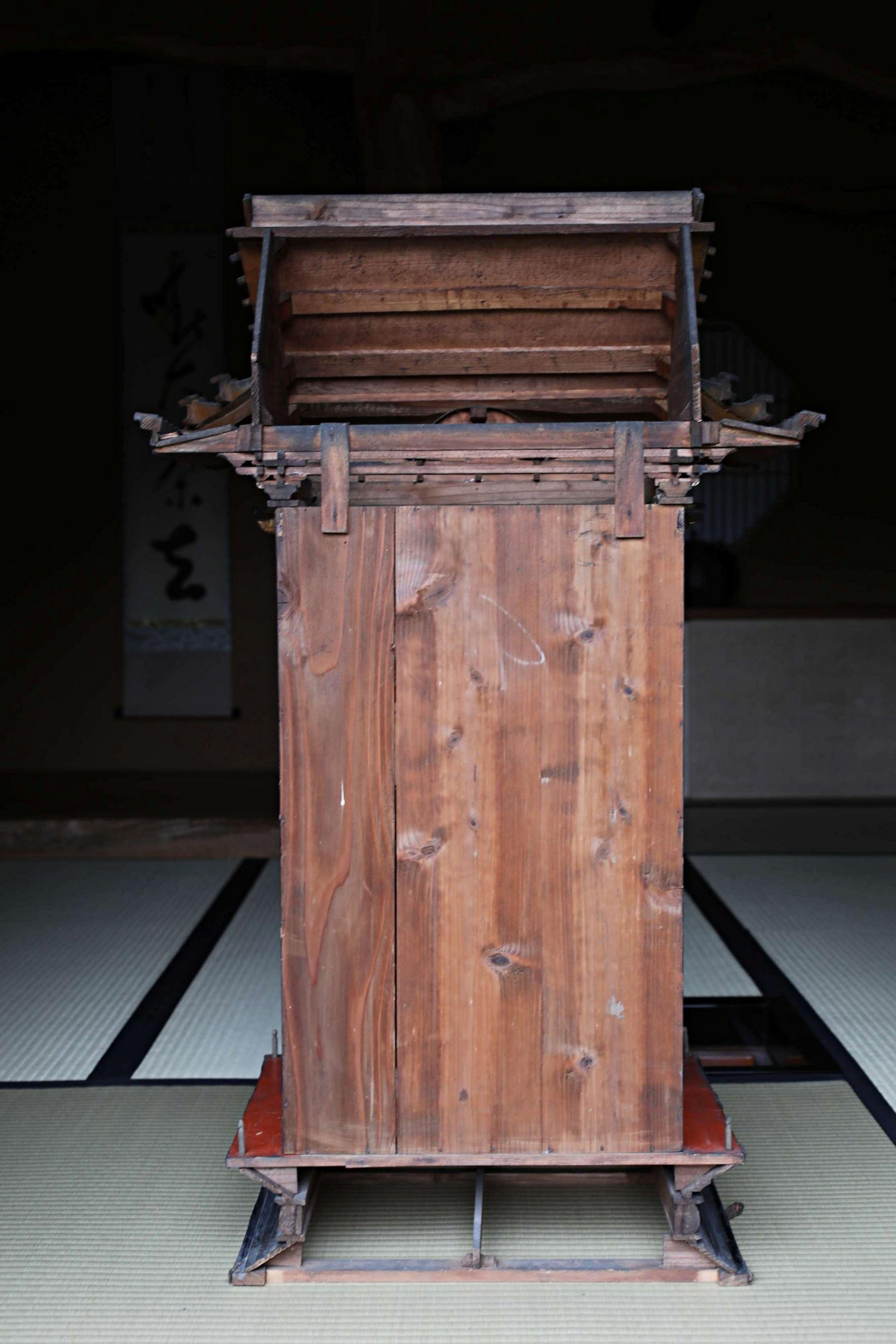a wooden structure with a sloping roof, possibly a traditional Japanese building, placed on a tatami mat floor.