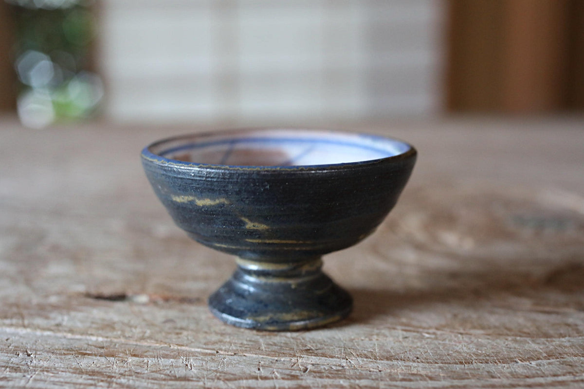 A small, black ceramic bowl with a blue rim sits on a wooden surface.