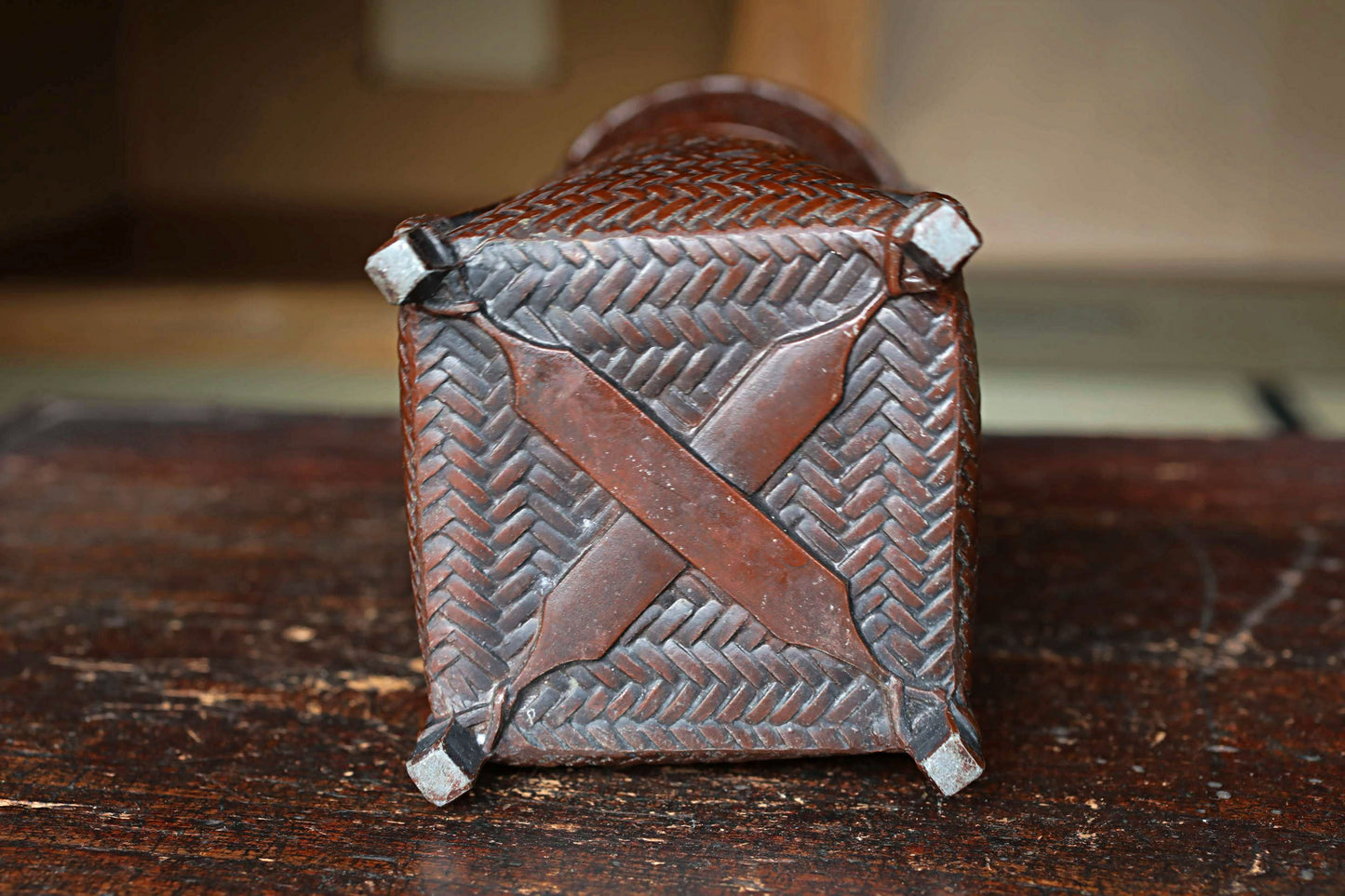 A close-up view of the back of a brown, woven basket or container with a distinctive X pattern.