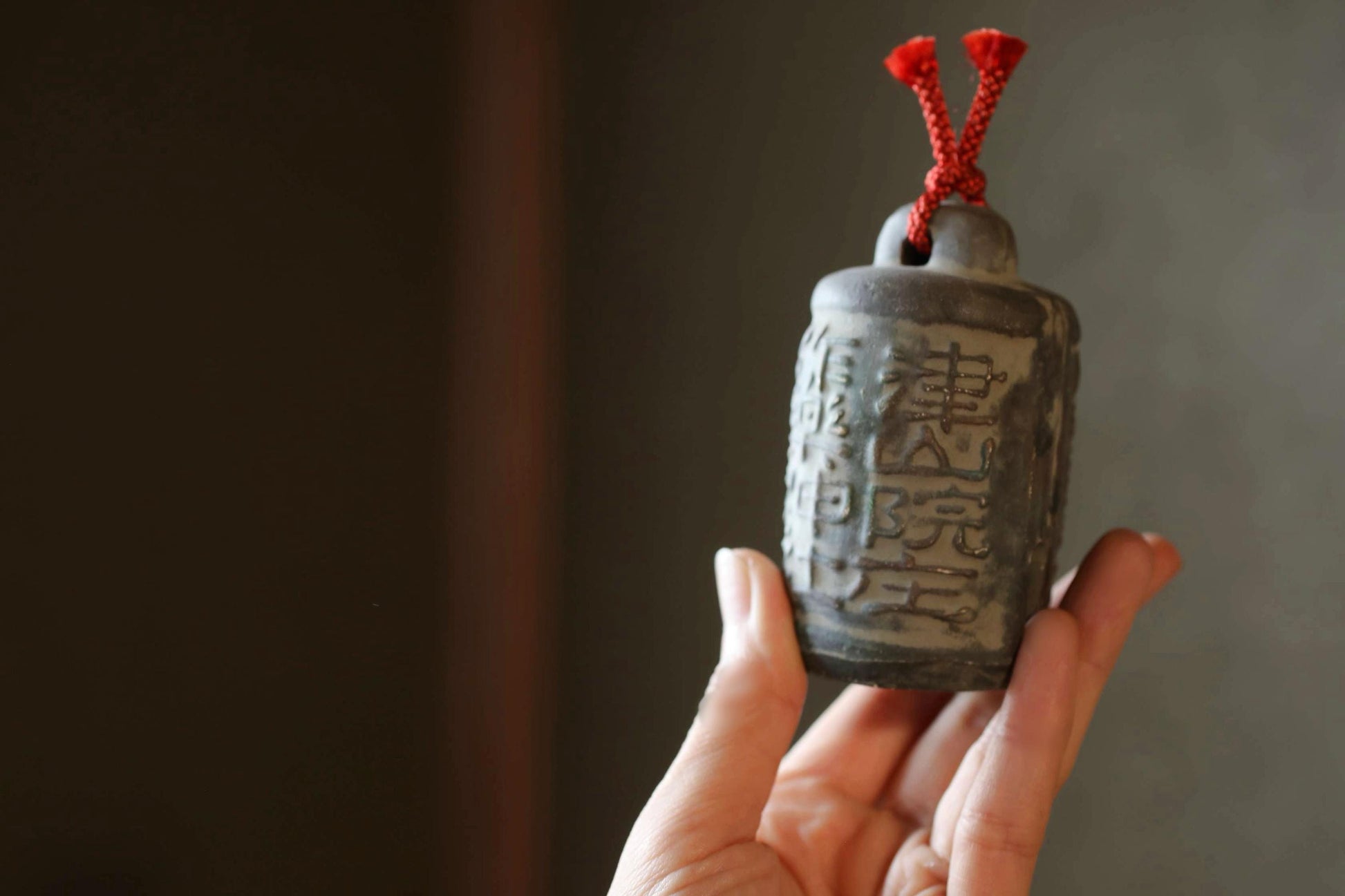 A hand holding a small gray ceramic object with red strings attached to it.
