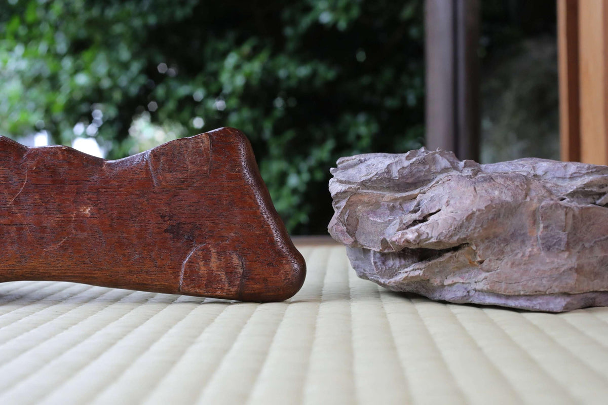 a wooden object with a curved shape and a large rock with a jagged surface placed on a textured surface.