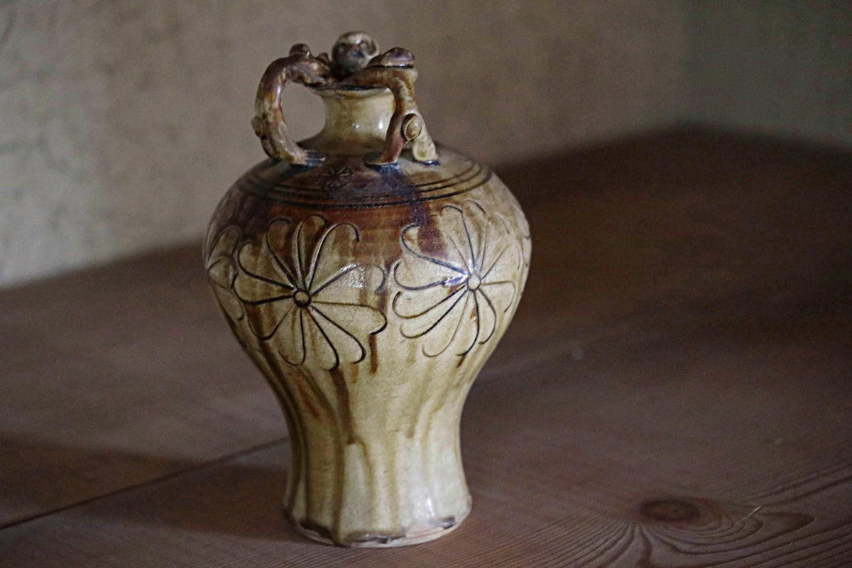A ceramic vase with a floral design sits on a wooden surface.