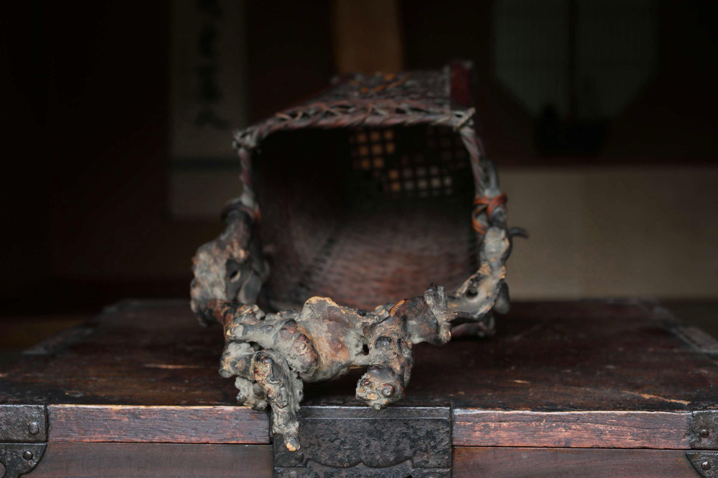 An antique, weathered metal object with a carved design sits on a wooden surface, with a blurred background.