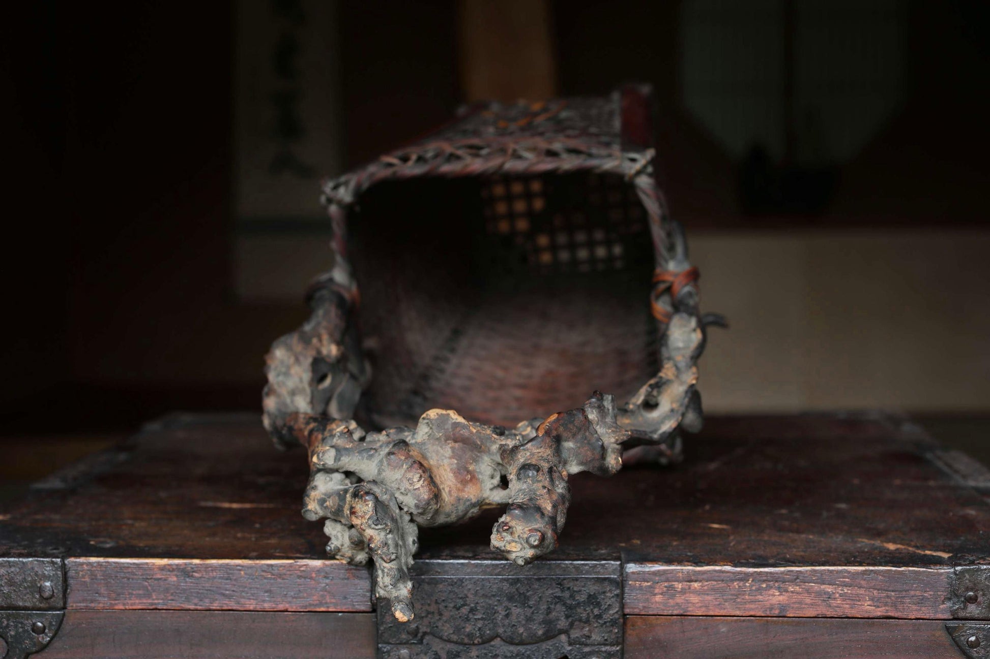 An antique, weathered metal object with a carved design sits on a wooden surface, with a blurred background.