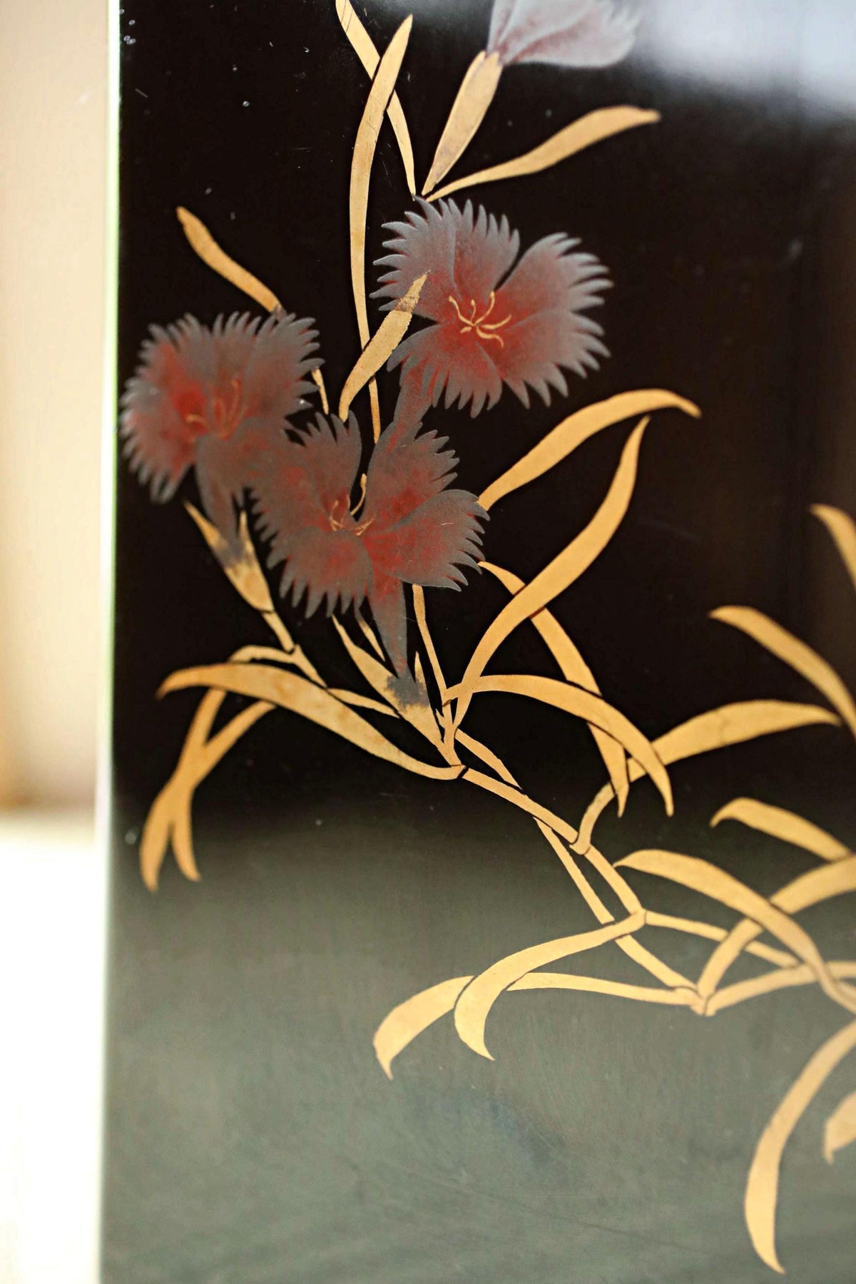 a close-up view of a black surface with a floral design in gold. The design consists of three red flowers with long, thin petals against a dark background.