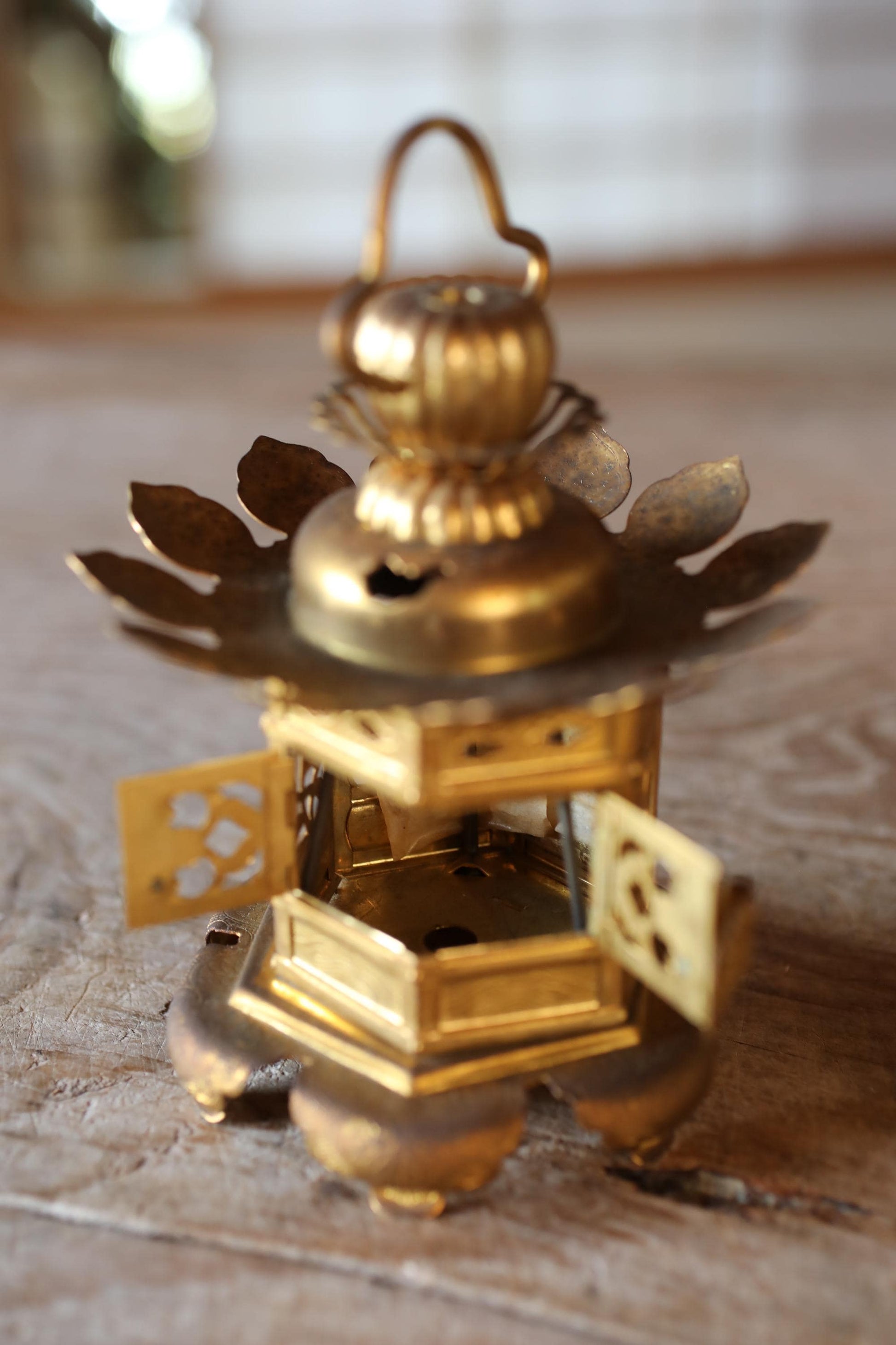 A small, ornate brass lantern with a pointed top and intricate designs, sitting on a wooden surface.