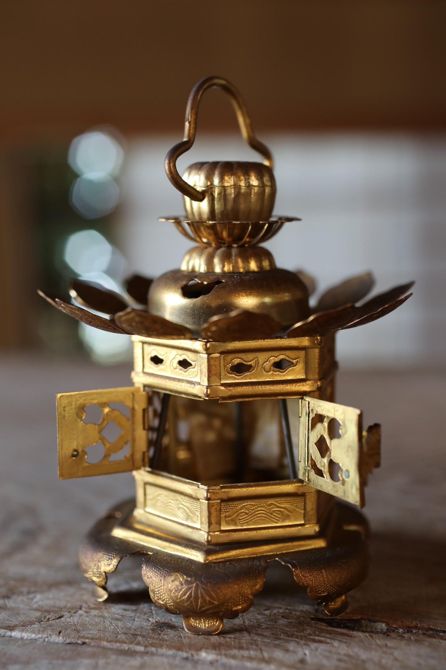 A golden, ornate lantern with intricate designs and a curved handle, sitting on a wooden surface.