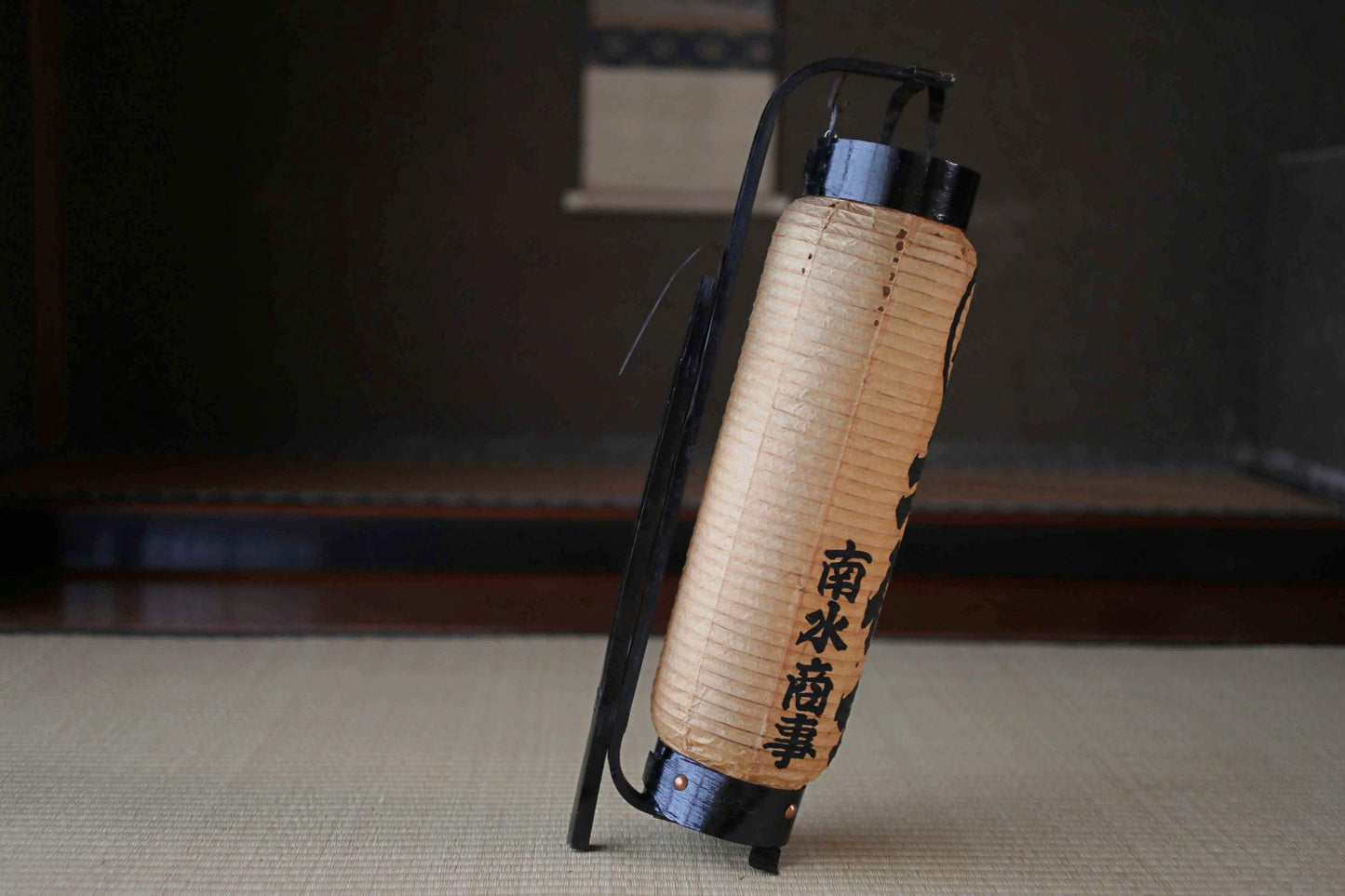 A traditional Japanese paper lantern with Chinese characters on it, standing on a tatami mat.