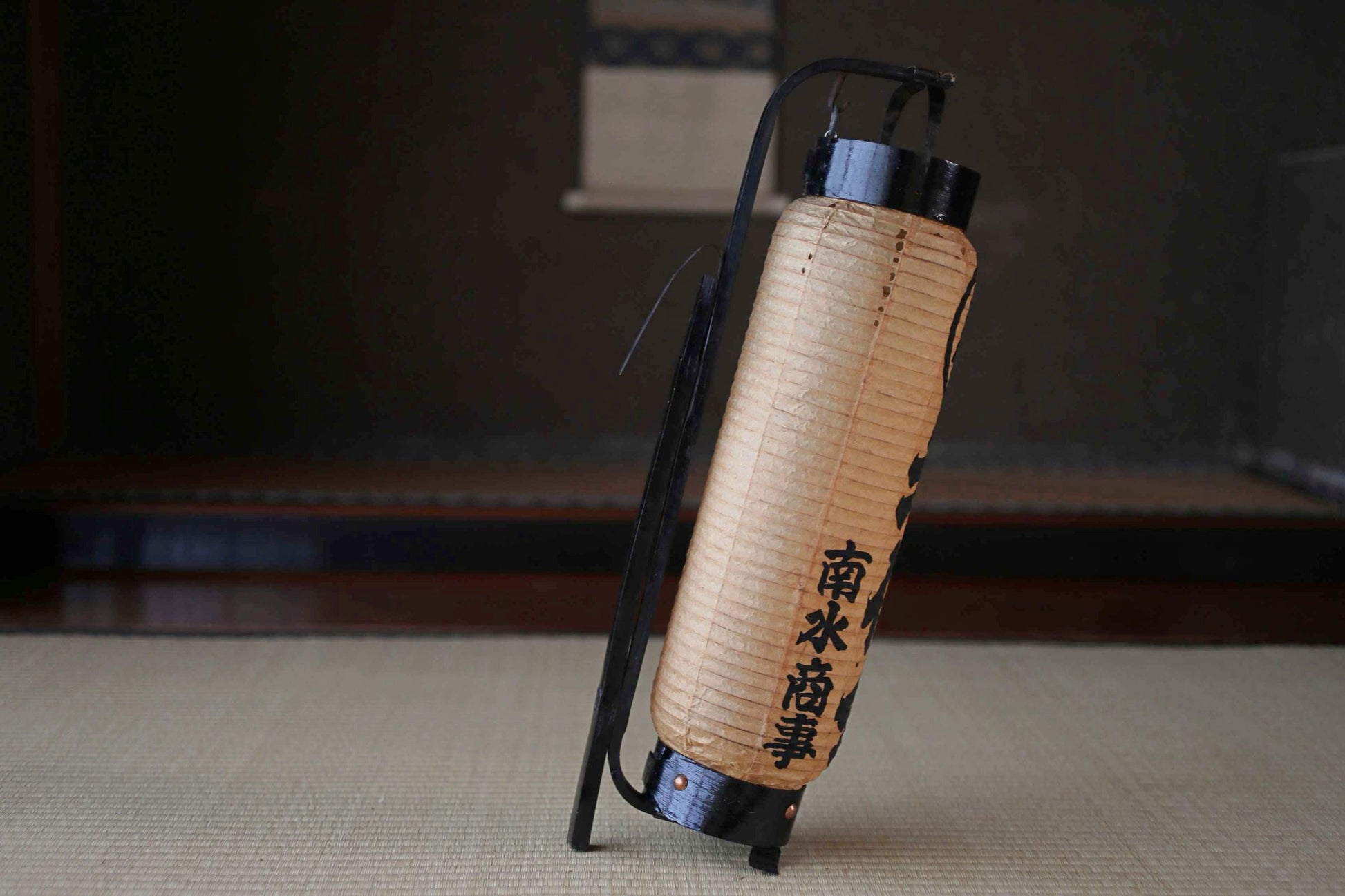 A traditional Japanese paper lantern with Chinese characters on it, standing on a tatami mat.