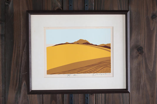 The image is a framed artwork depicting a landscape with a yellow field and a mountain range in the background.