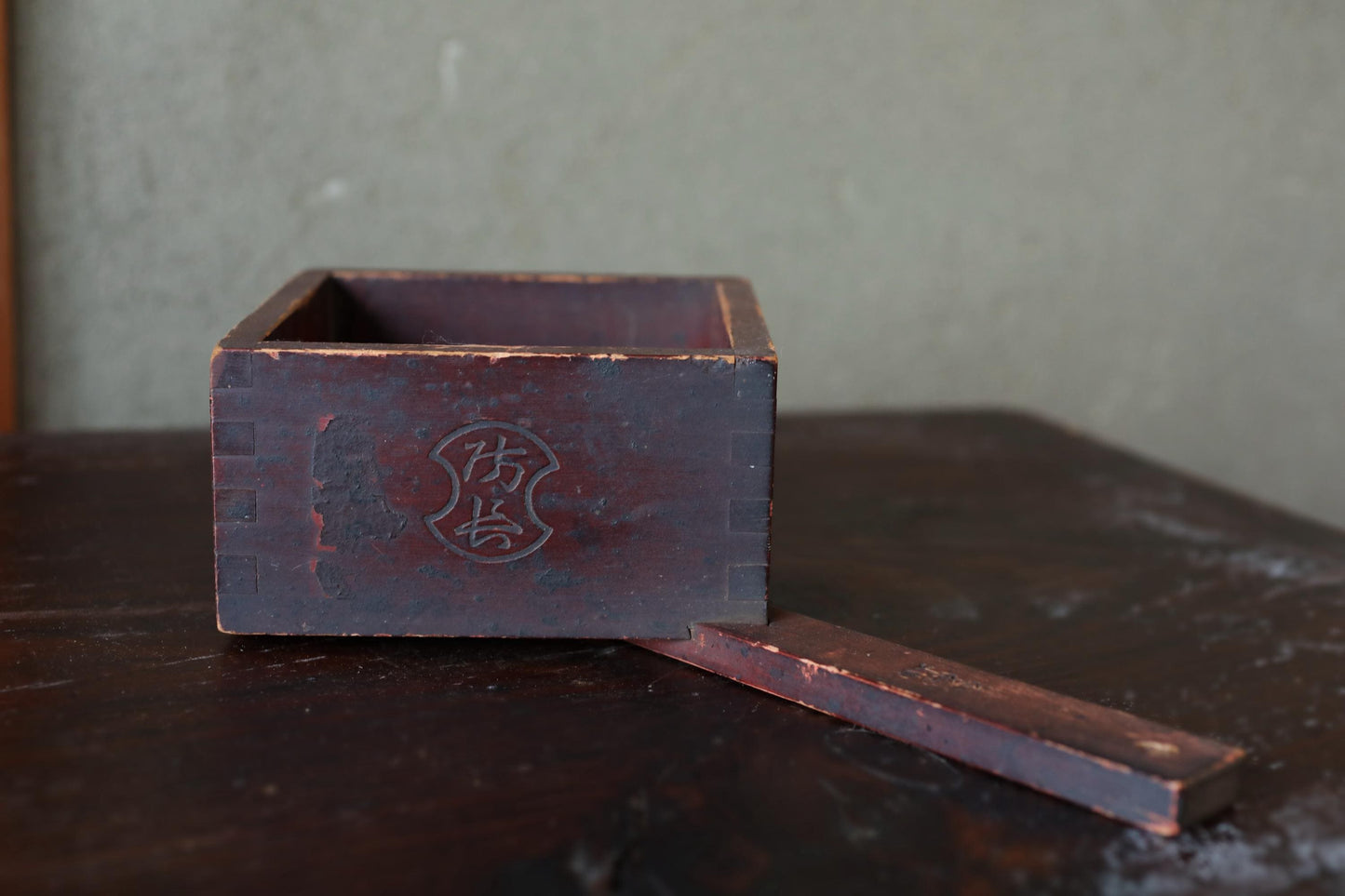An old, weathered wooden box with a carved design on its side, sitting on a dark wooden surface.