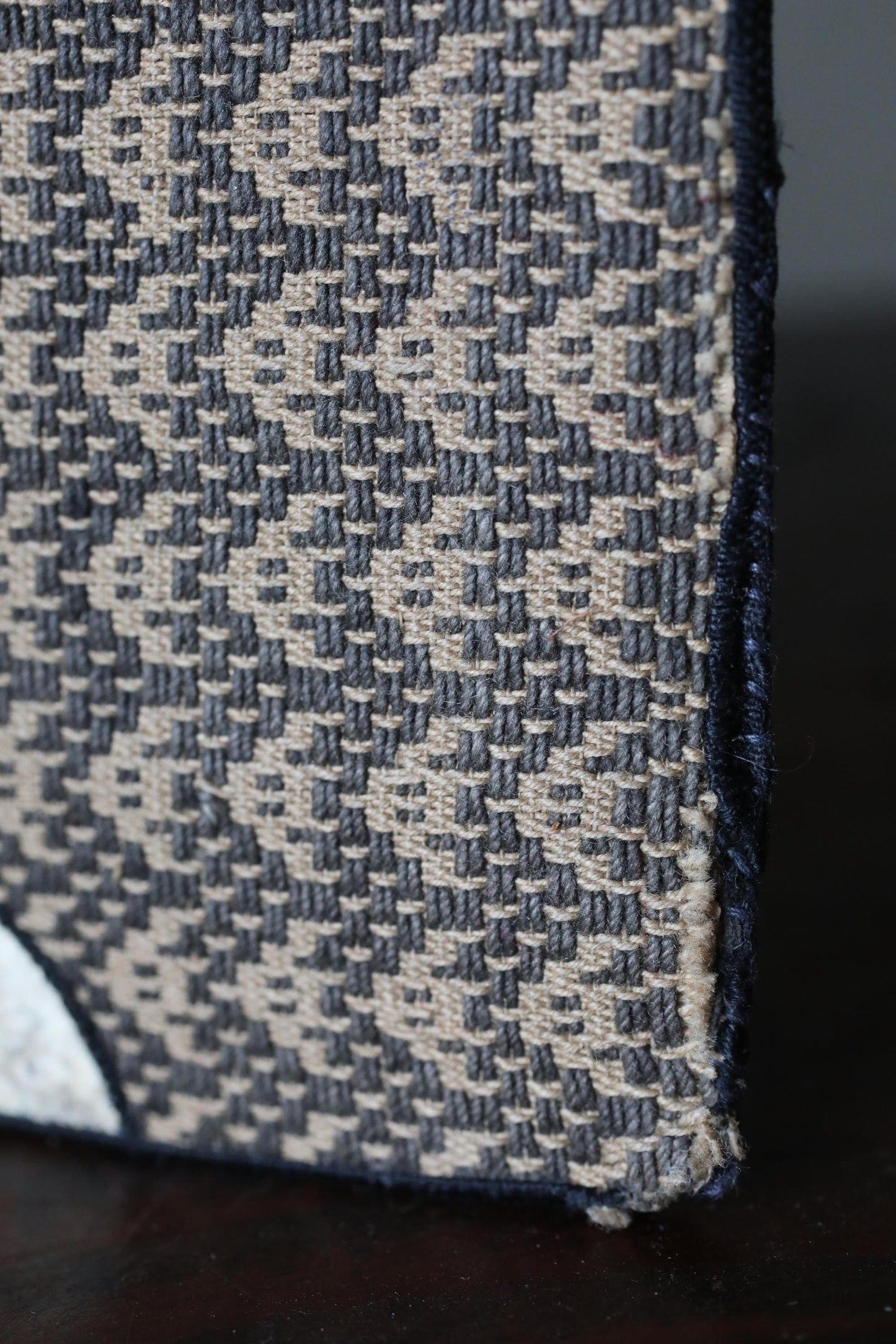 a close-up view of a textured fabric with a geometric pattern, featuring a mix of black, gray, and beige colors.