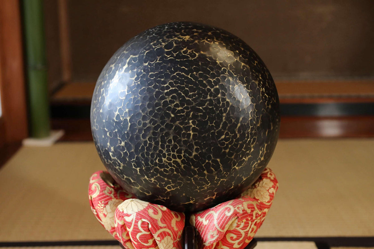 A close-up image of a black, textured ball resting on a red and white patterned cloth, with a blurred background.