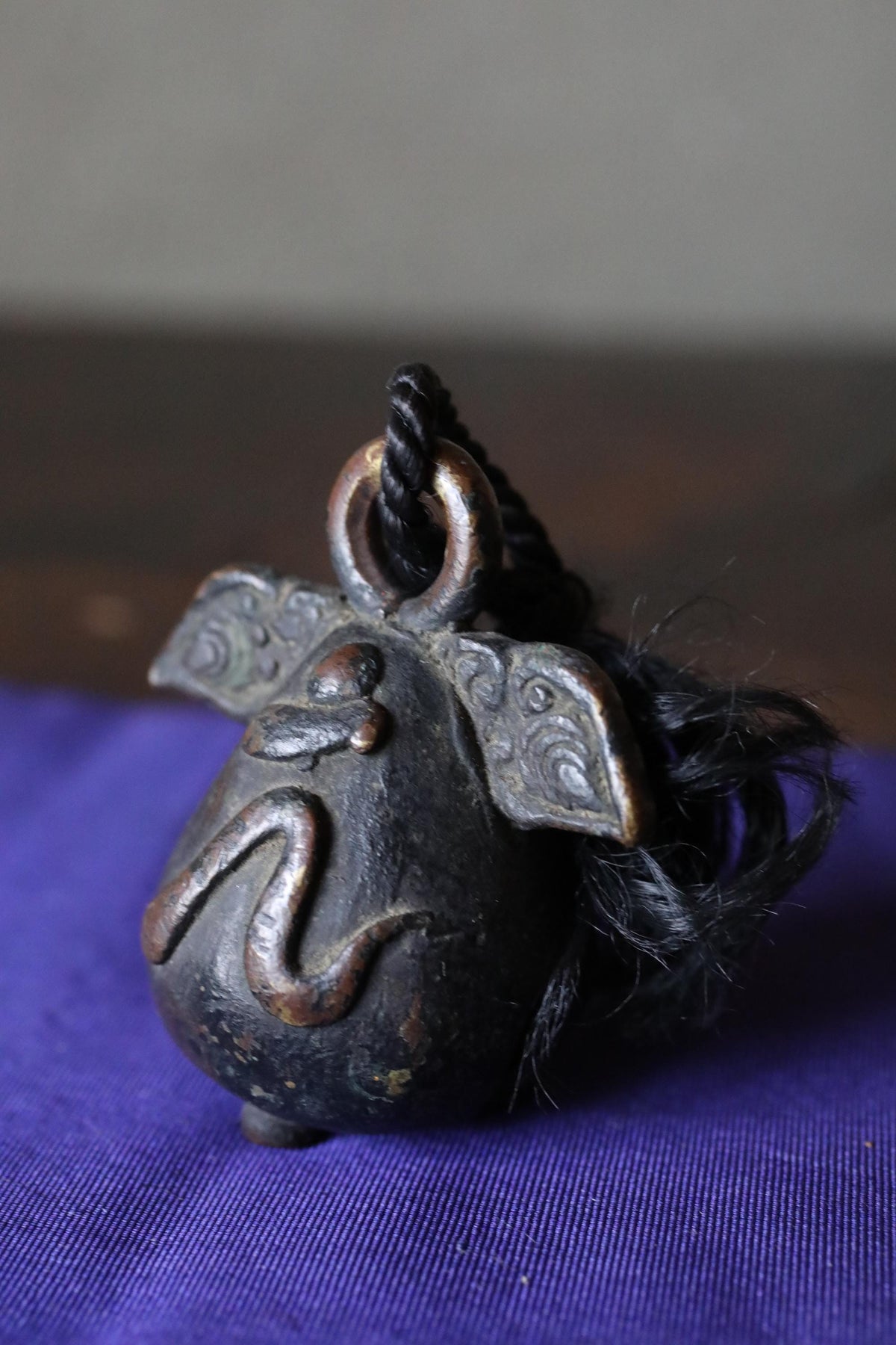 A black metal bell with a twisted cord hanging from it, sitting on a blue surface.