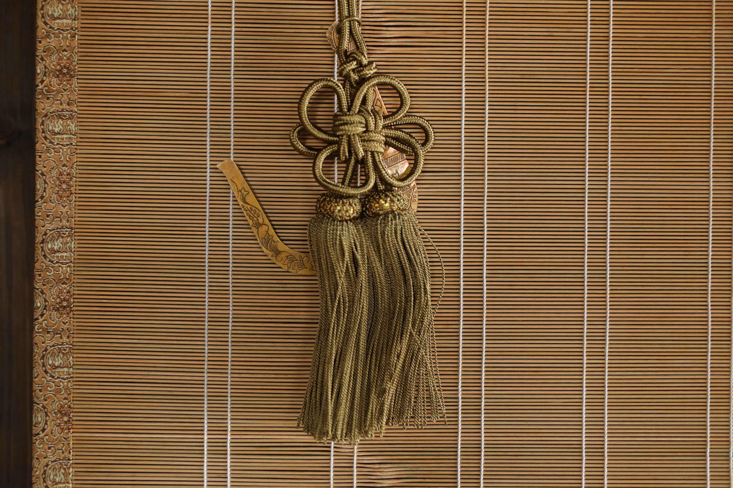 A decorative tassel hanging on a bamboo blind, featuring a floral design and gold accents.
