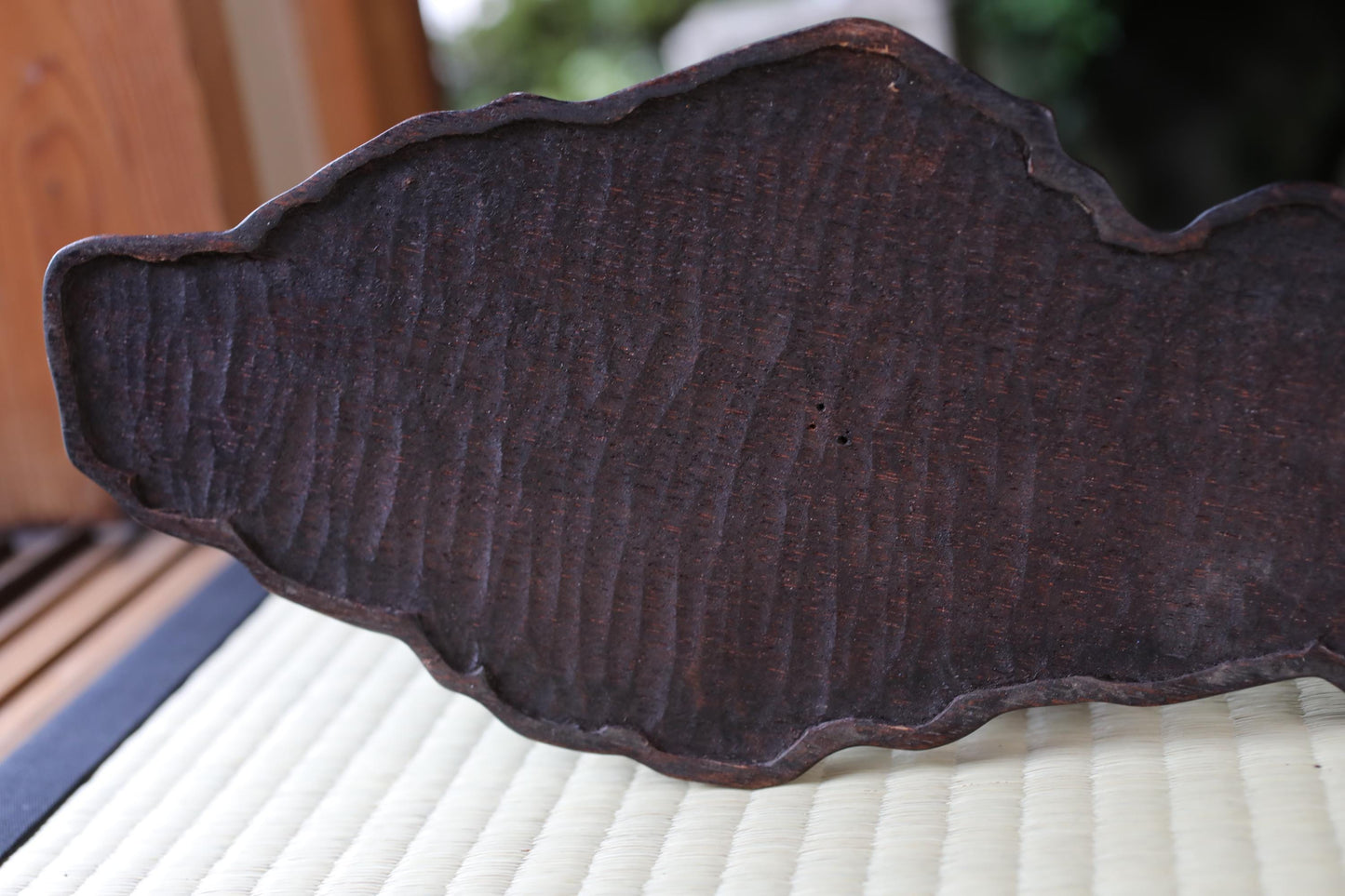 a close-up view of a dark, textured surface, possibly a piece of wood or metal, with a blurred background.