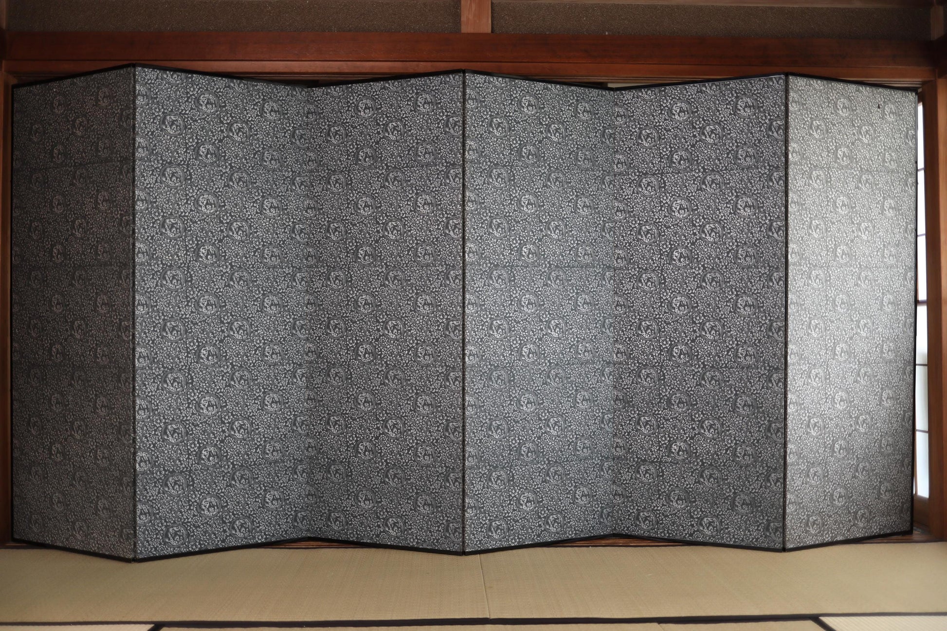 a large, multi-paneled folding screen or partition with a repeating pattern of black and white designs. The screen is folded in half, revealing its structure and design.