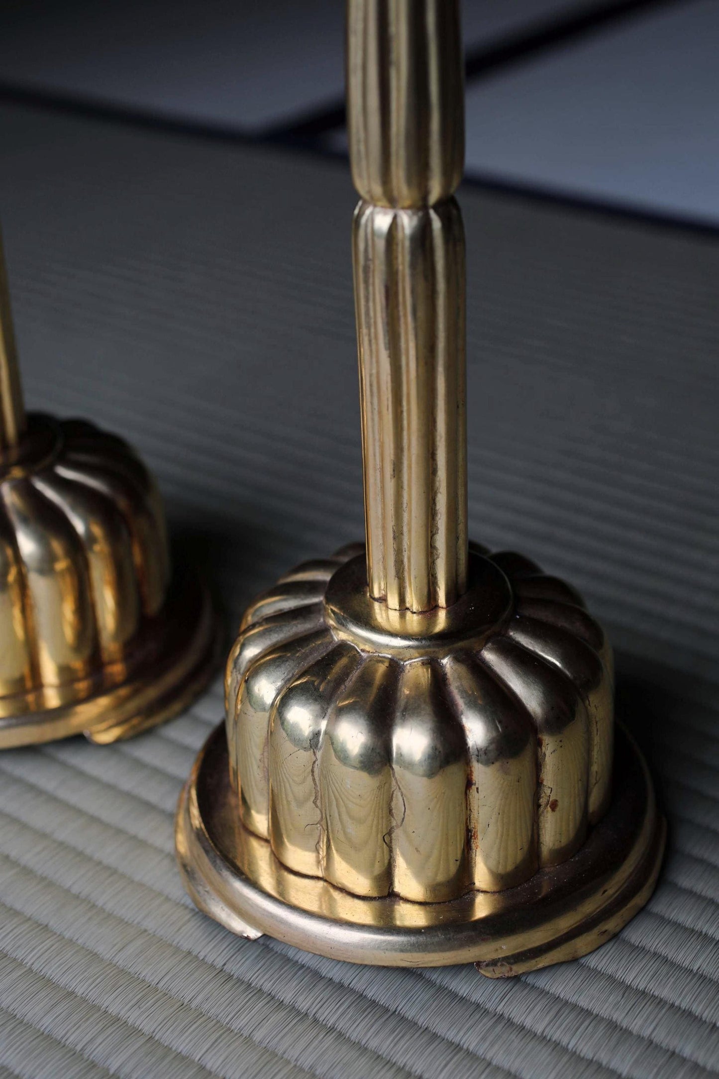 a pair of ornate brass candlesticks with a scalloped design on their bases, placed on a textured surface.