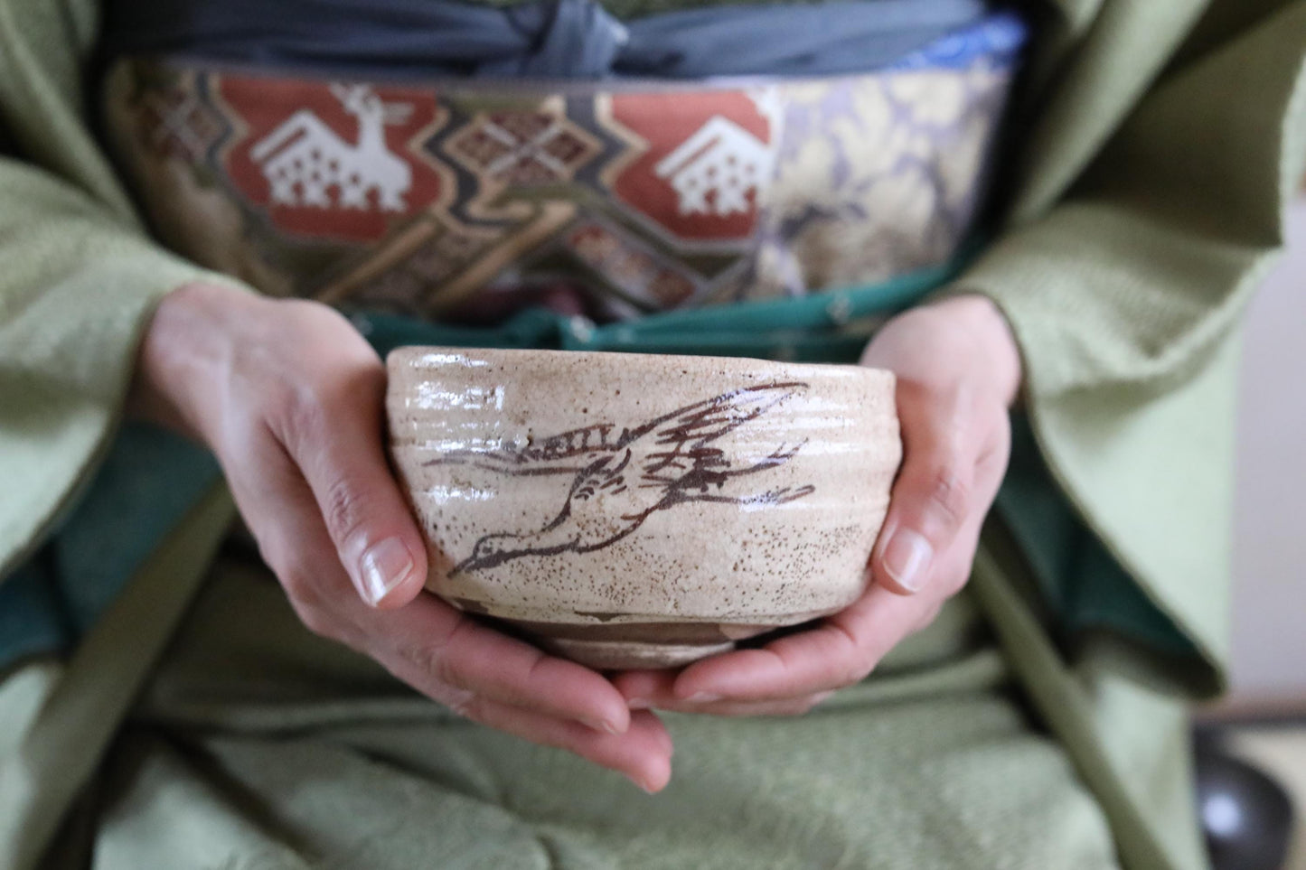 A person's hands holding a ceramic bowl with a bird design on it.