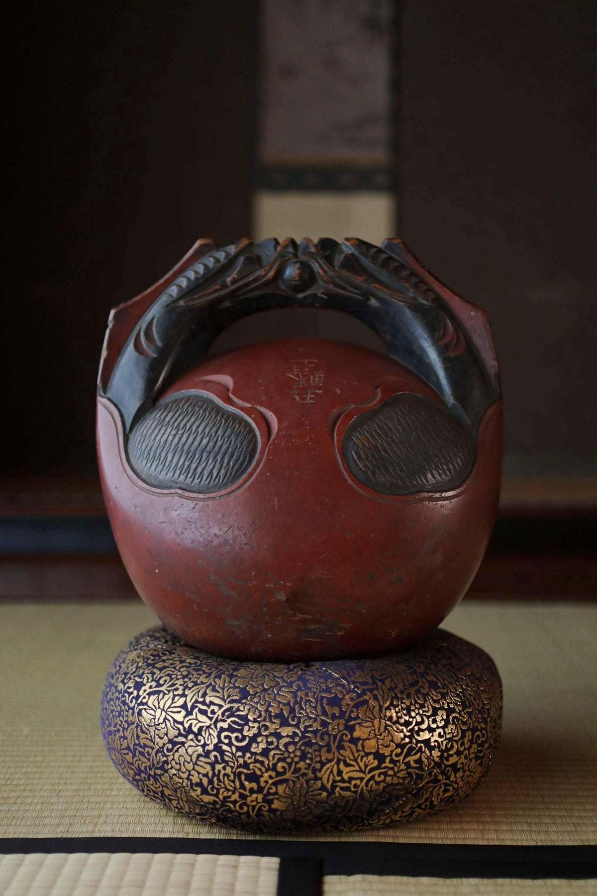 A red and black ceramic object with a carved handle, sitting on a blue and gold decorative base.