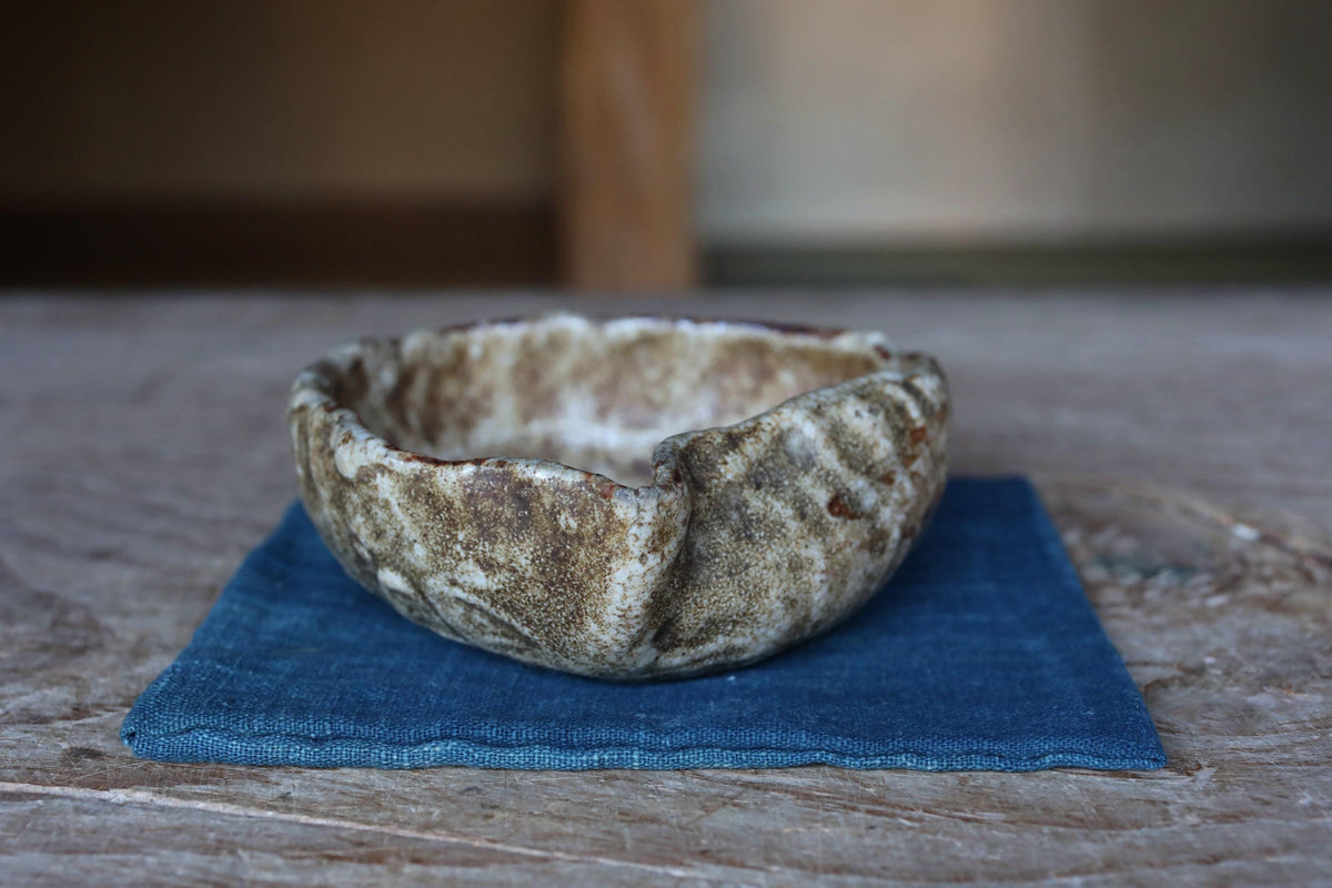 A ceramic bowl with a textured surface sits on a blue cloth on a wooden surface.
