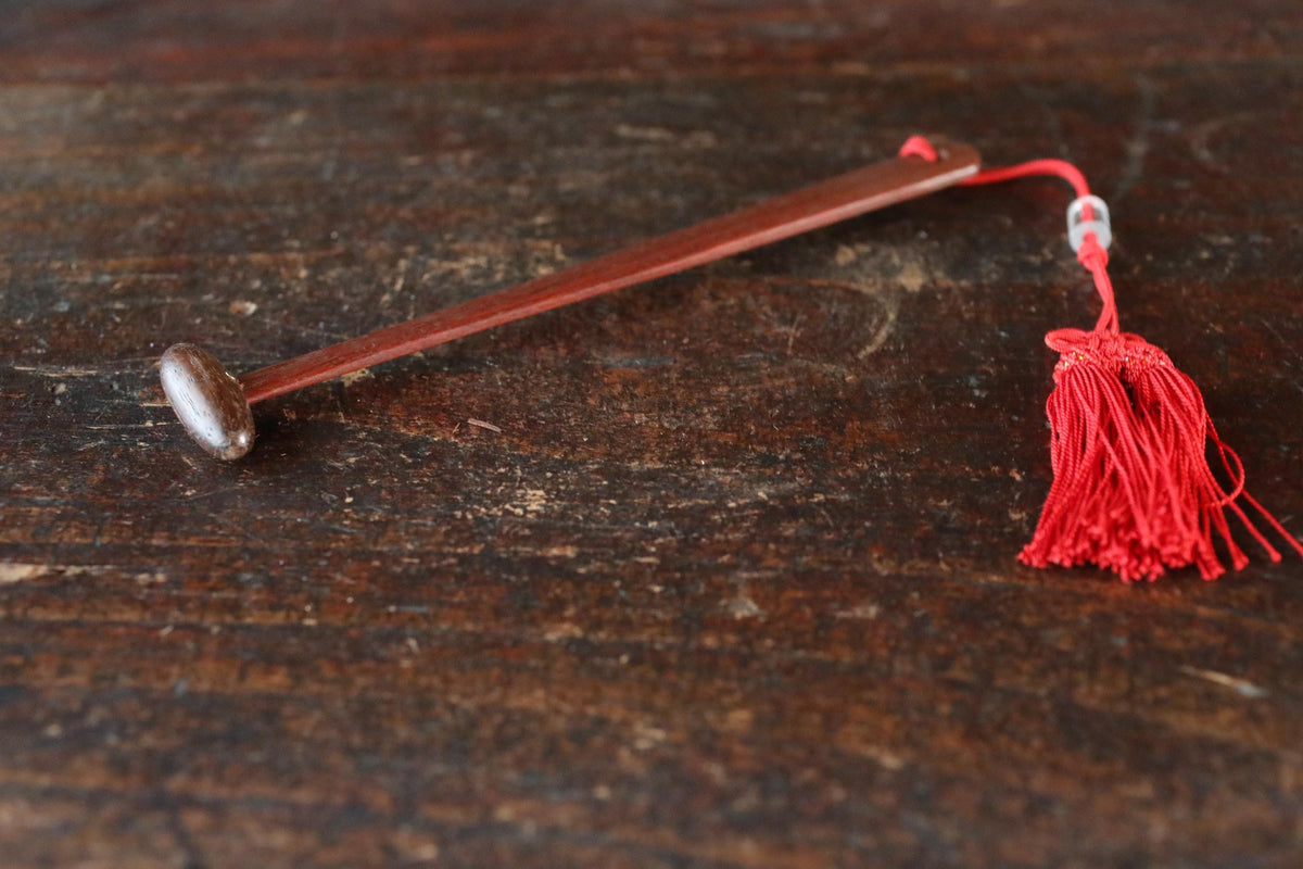 A red tassel with a metal object attached to it is resting on a wooden surface.