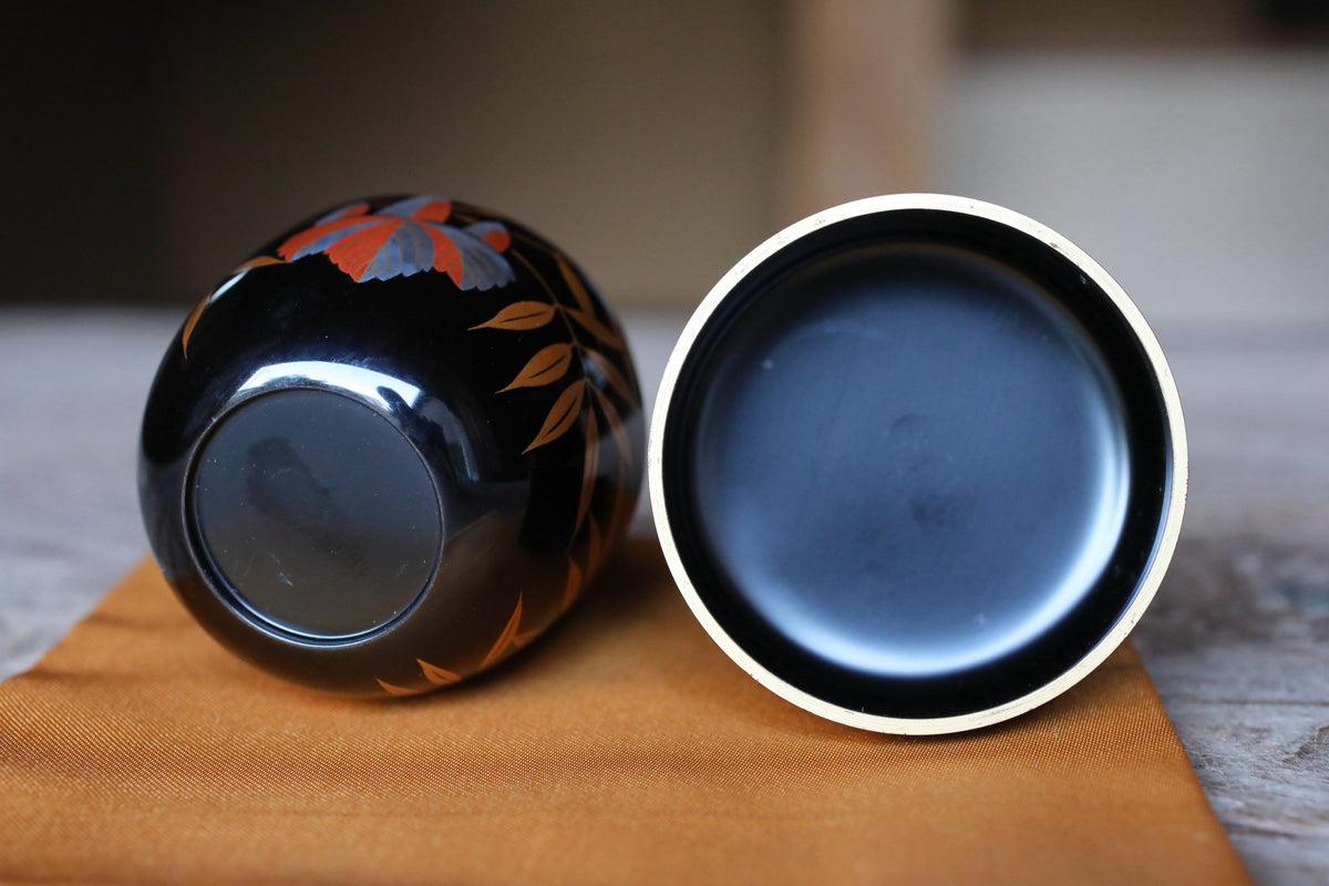 two black vases with orange and gray leaf designs on them, placed on a wooden surface.
