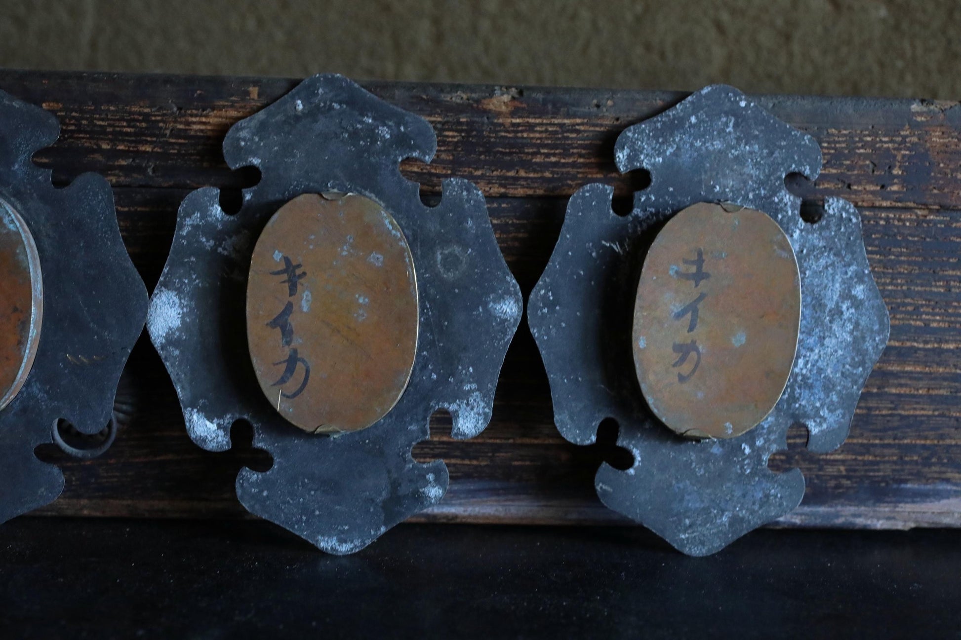a close-up view of a wooden surface with several metal objects attached to it, including two oval-shaped metal pieces with Japanese characters on them.