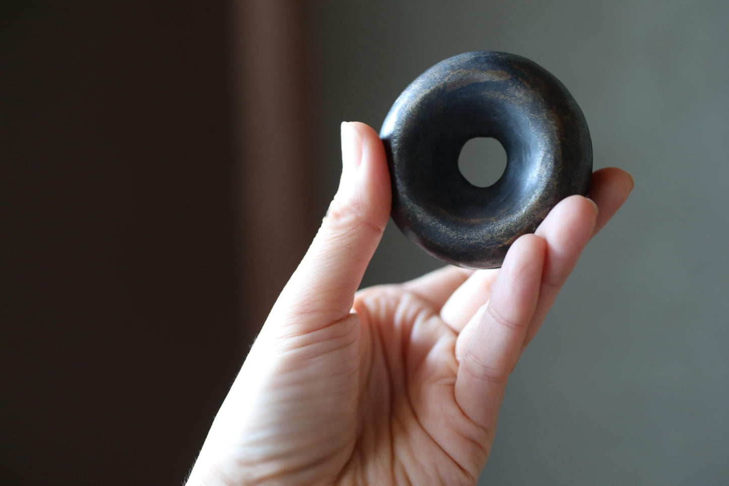 A hand holding a black, round object with a hole in the center, against a blurred background.