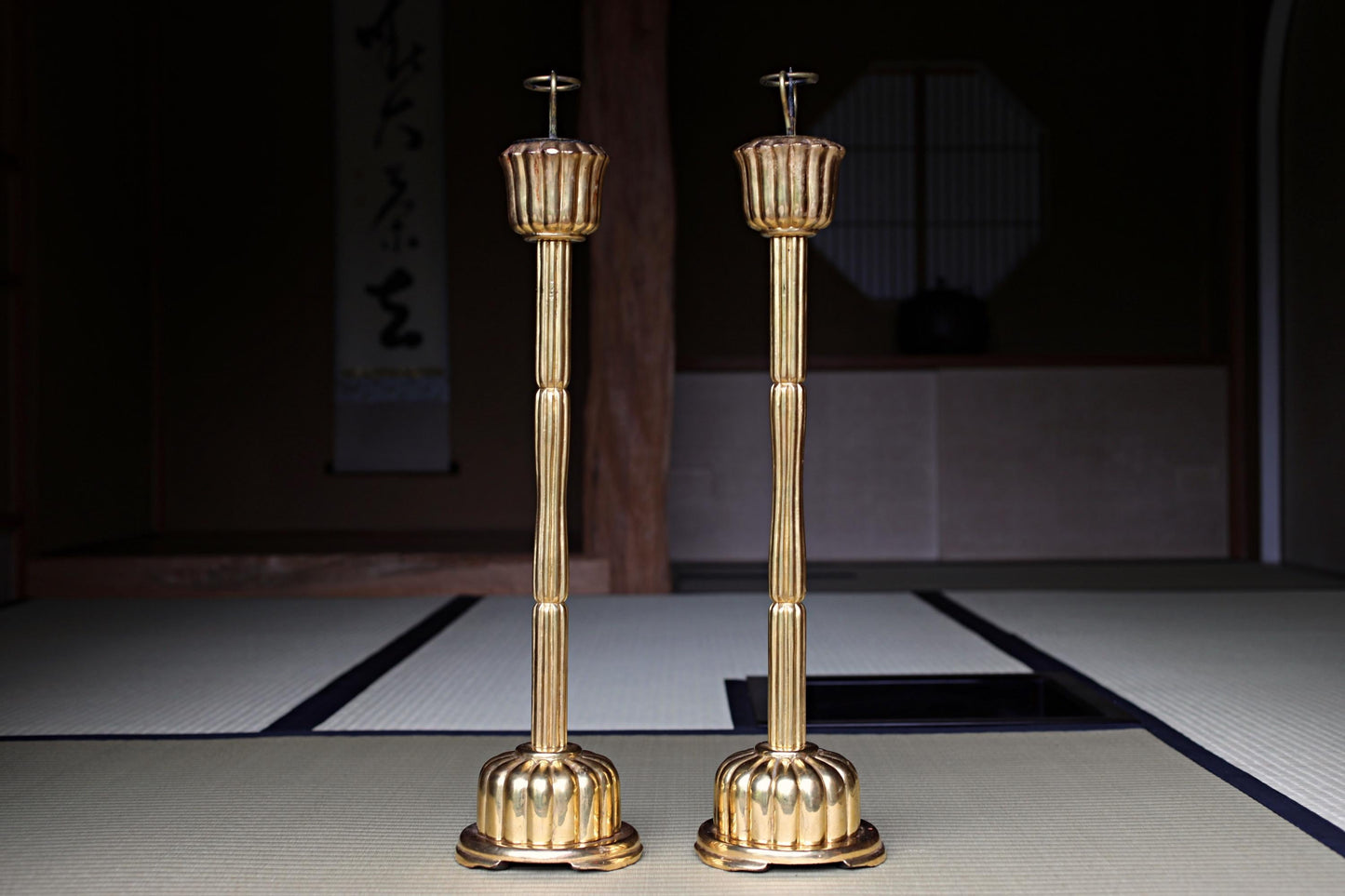 two golden candlesticks standing side by side on a white mat.